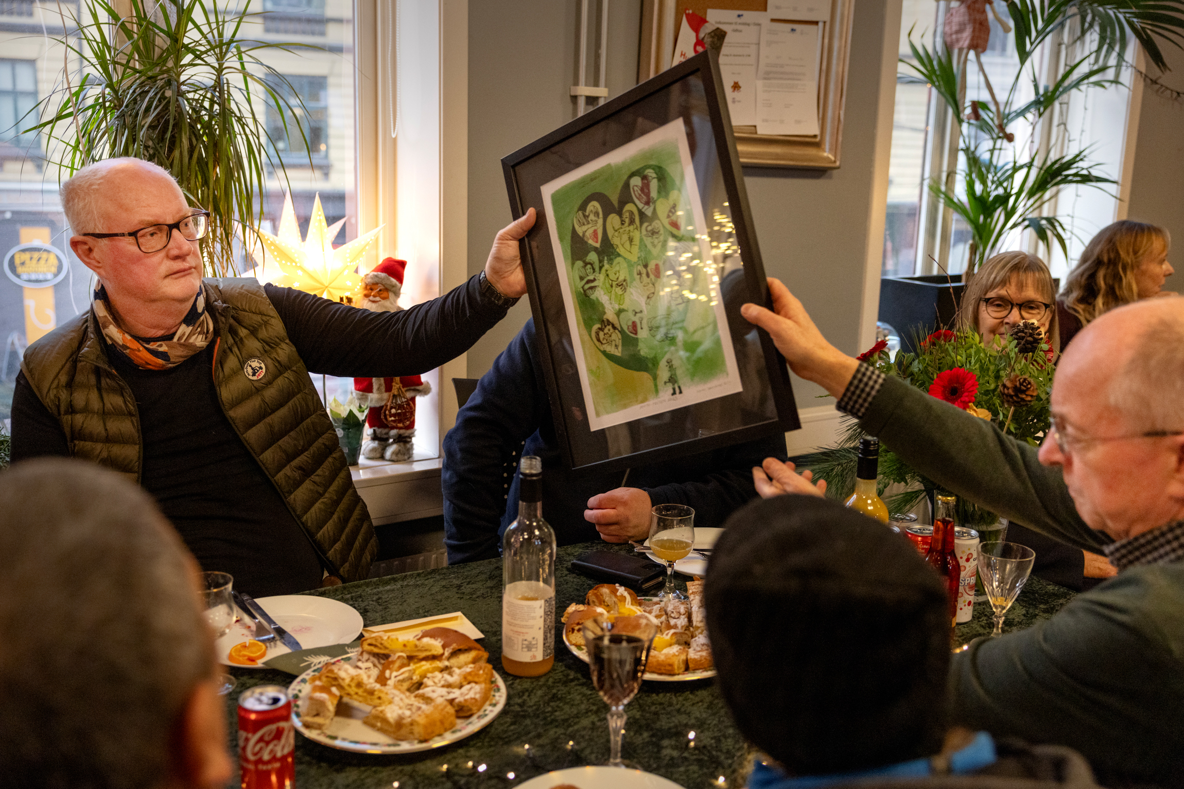 På tvers av bordet med mat holder to menn begge i et grønt bilde med svart ramme og passepartouter.