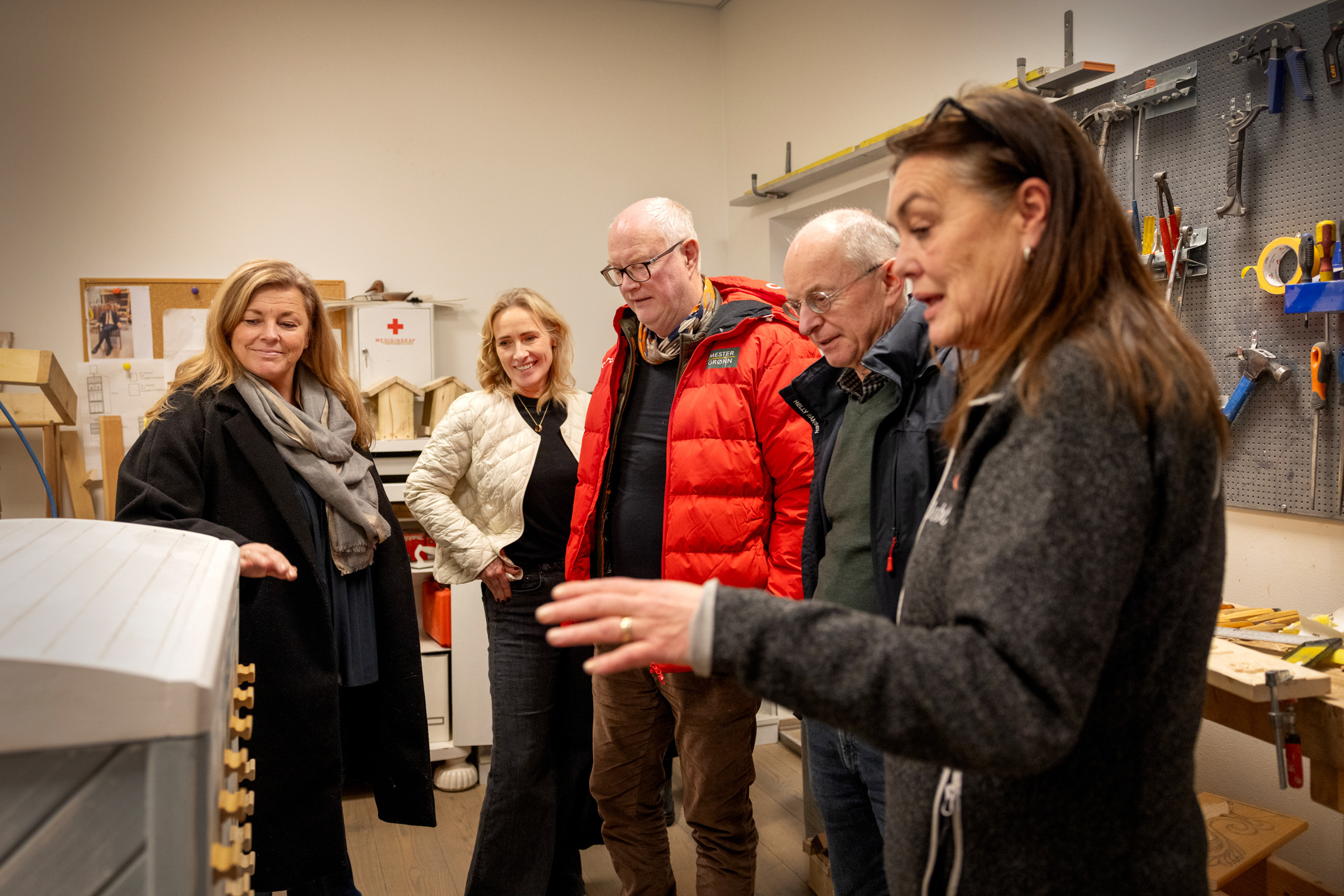 Kvinne med langt, brunt hår viser to kvinner og to menn en avansert maskin i verkstedet.