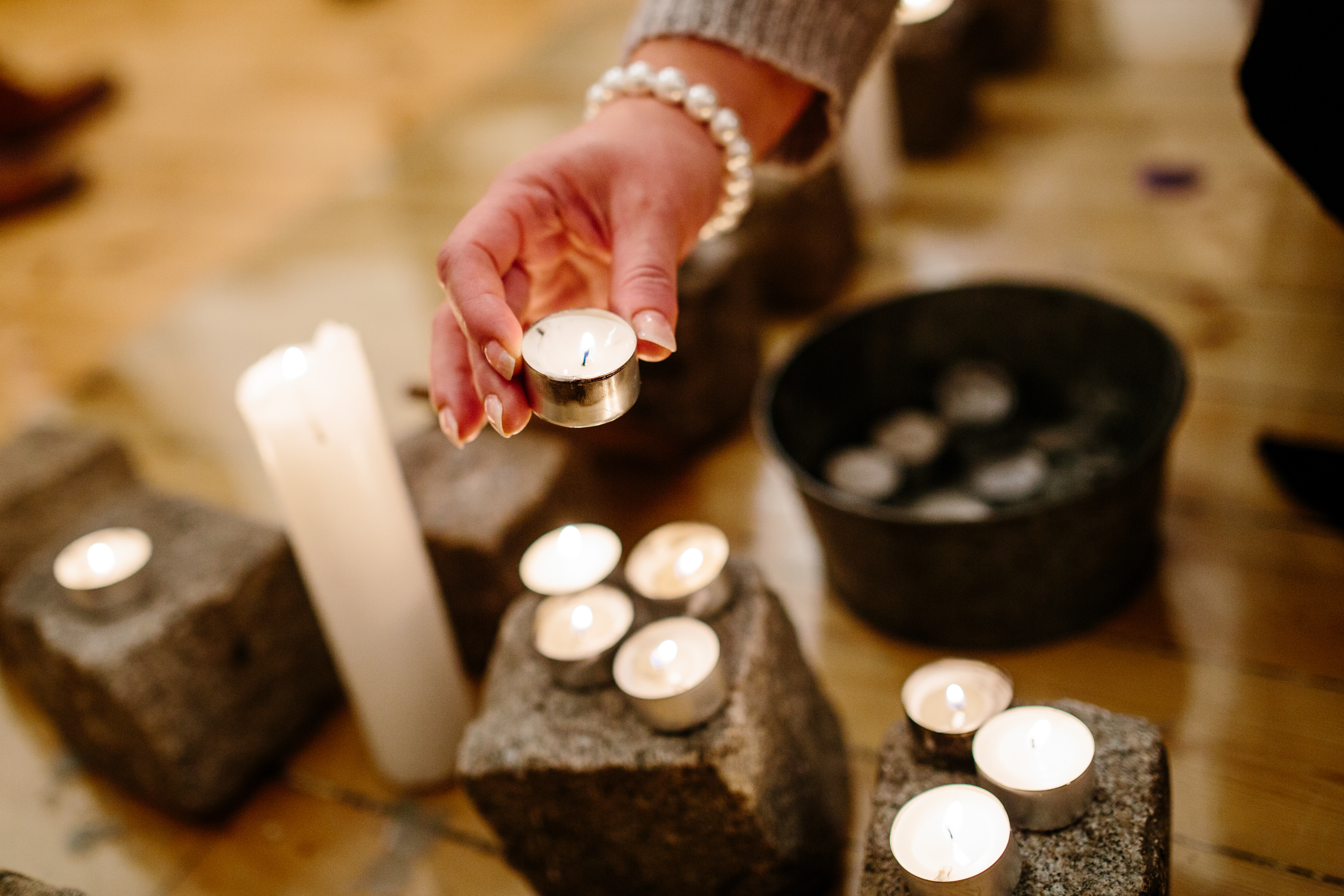 En hånd setter på plass et tent telys. Rundt står flere telys på brosteiner innendørs i ulike høyder