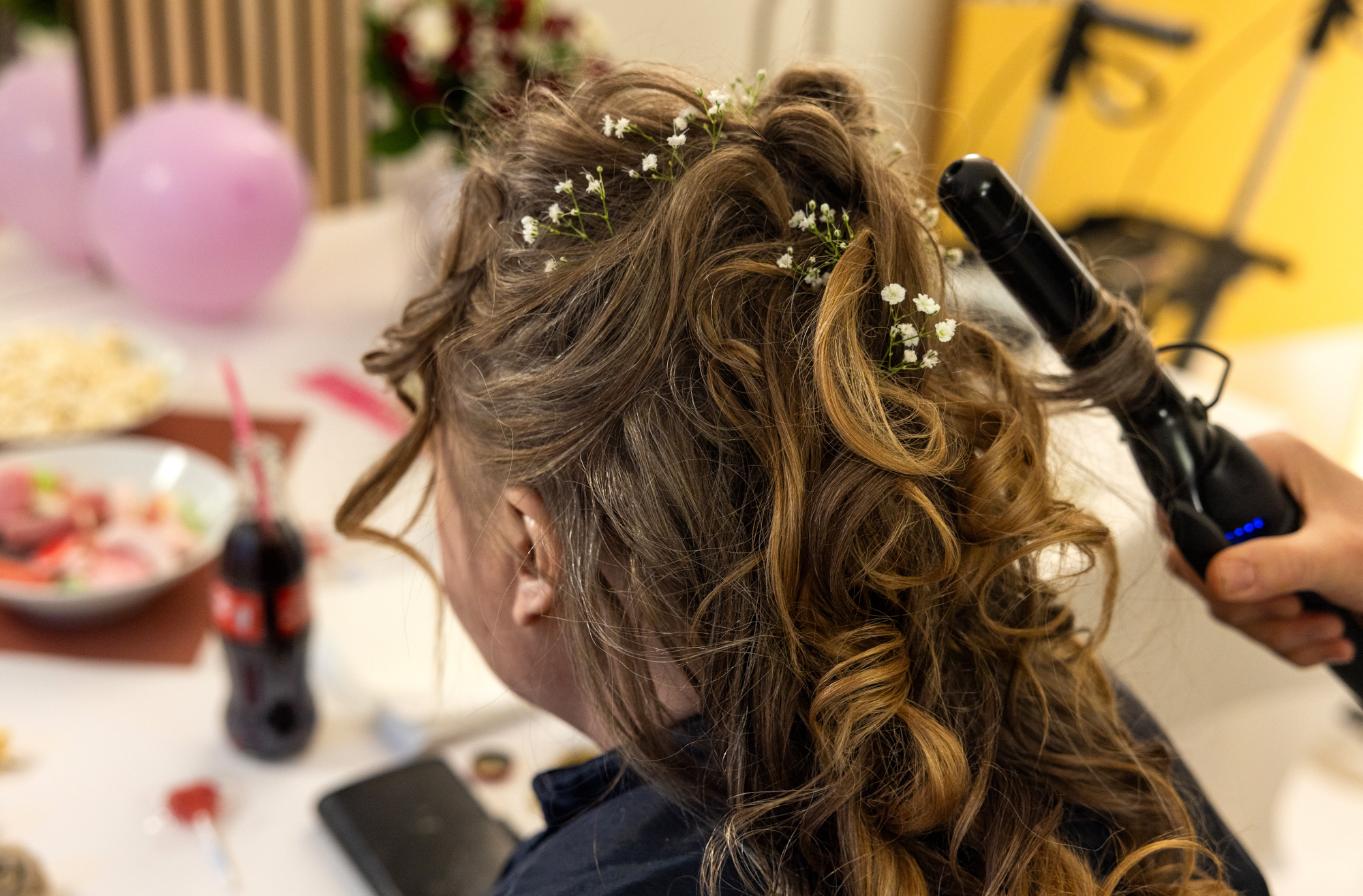 Foto: Håret som krølles med tang. Flere steder er det pyntet med hvite blomster. På bordet foran står det godteskåler.