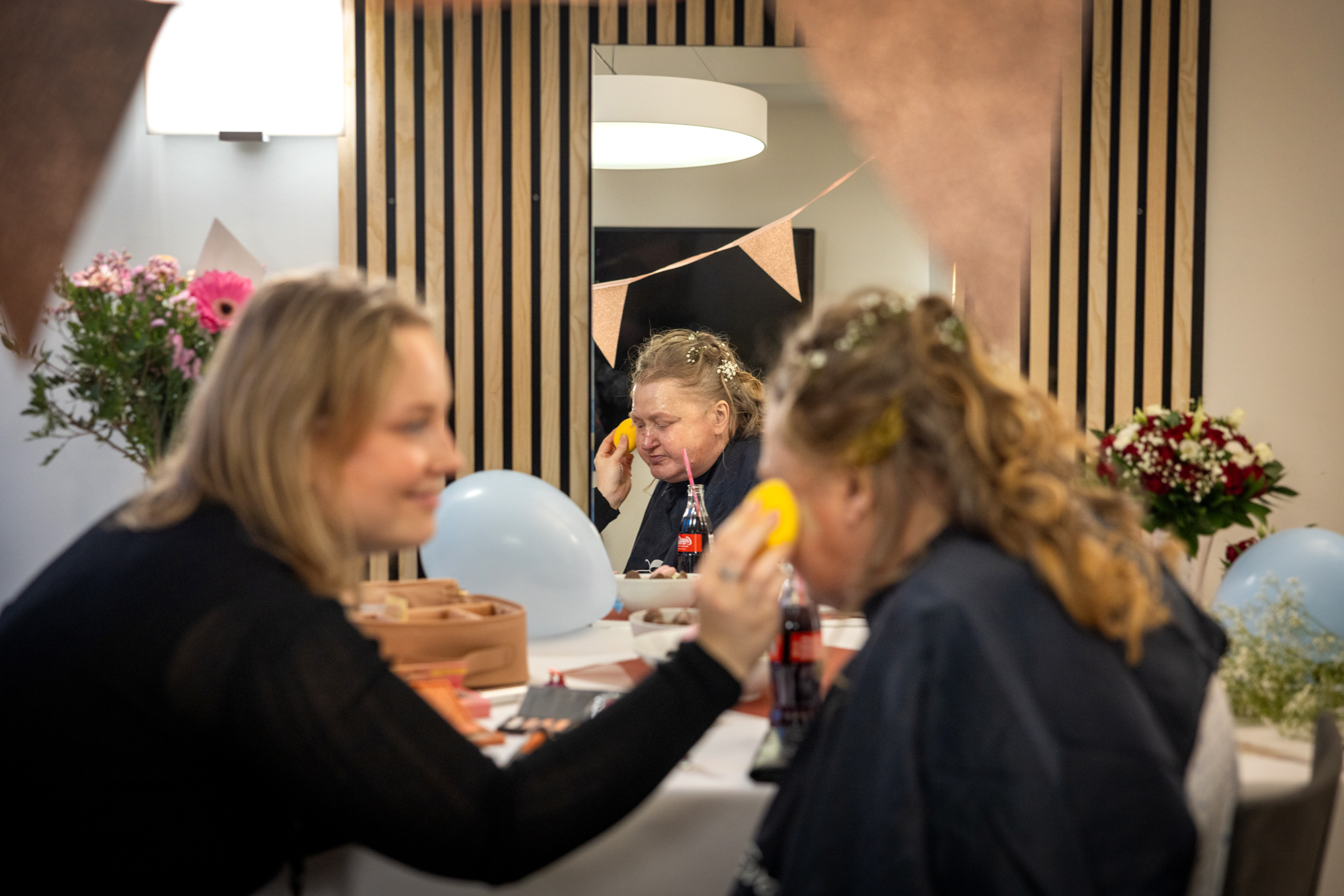 Foto: Yngre kvinne sminker en 20 år eldre kvinne. I bakgrunnen kan en se ting klart i et speil, mens det er uklart i forgrunnen.