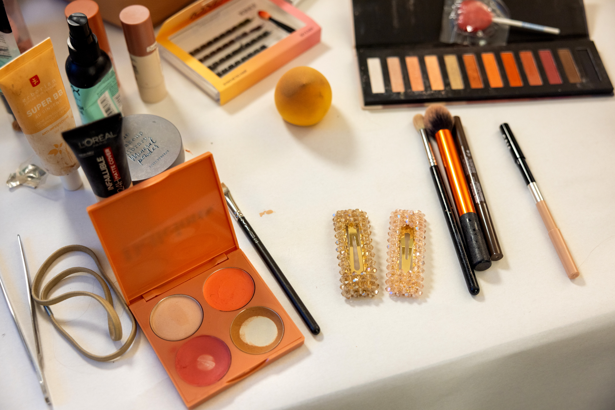 Foto: Sminkesaker, koster og kremer på et bort. Oppå den hvite duken ligger også et par glitrende hårspenner.