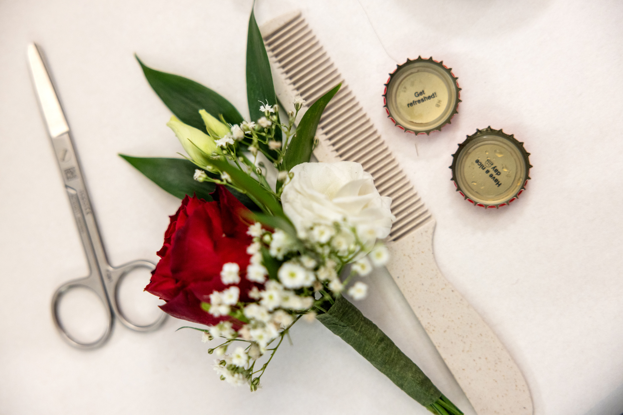 Foto: Utstyr til å klippe skjegg ligger på et hvitt bord sammen med en blomster til brystlommen og et par korker med tekst inni.