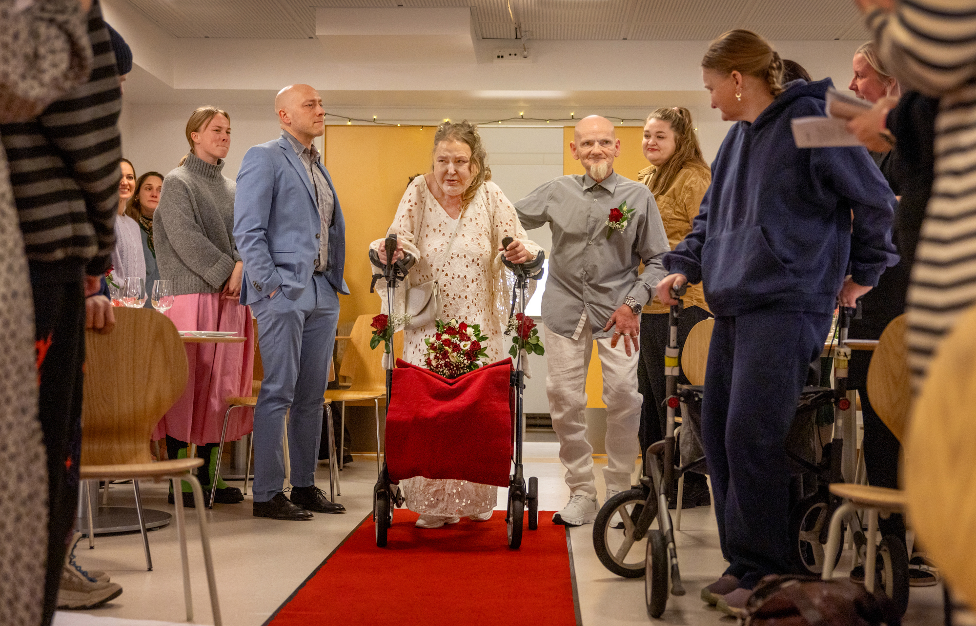 Foto: Mann og kvinne midt i livet går med rullator på et langt teppe.