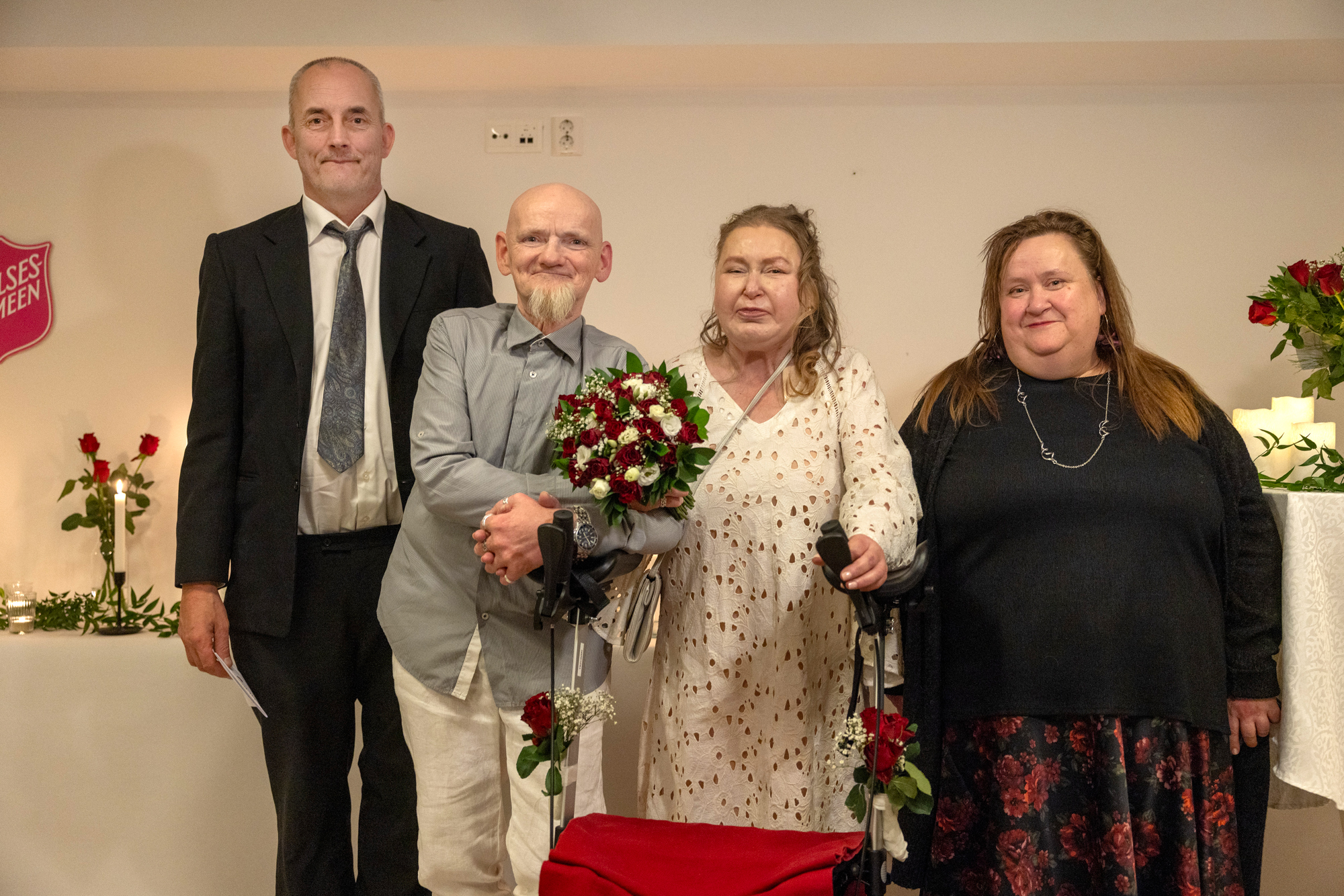 Foto: To menn og to kvinner står på rekke. De står etter høyde. I midten står brudeparet bak en rullator.