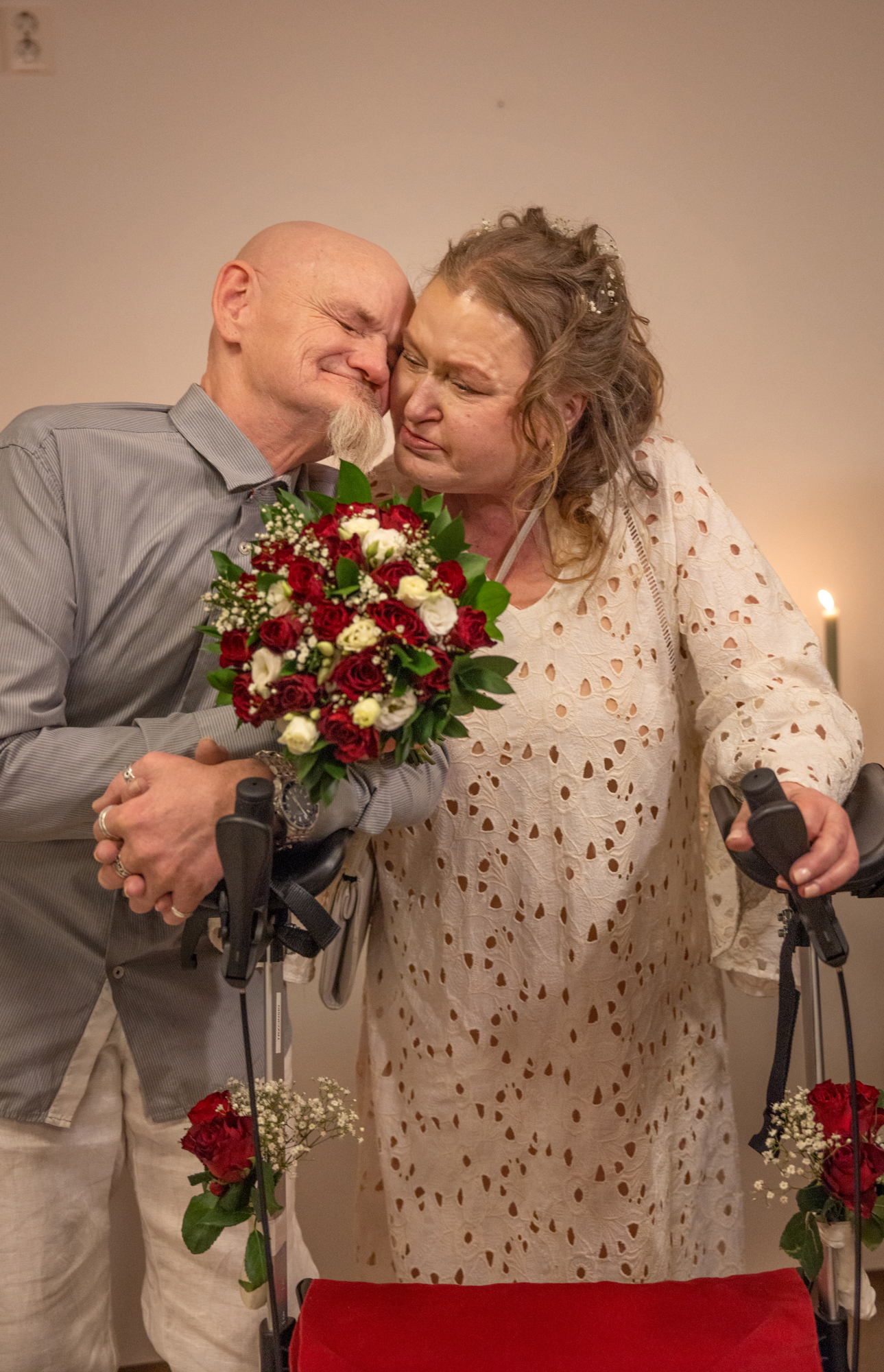 Foto: Mann uten hår og med flippskjegg gir en varm klem til en kvinne i kremfarget kjole som holder en brudebukett.