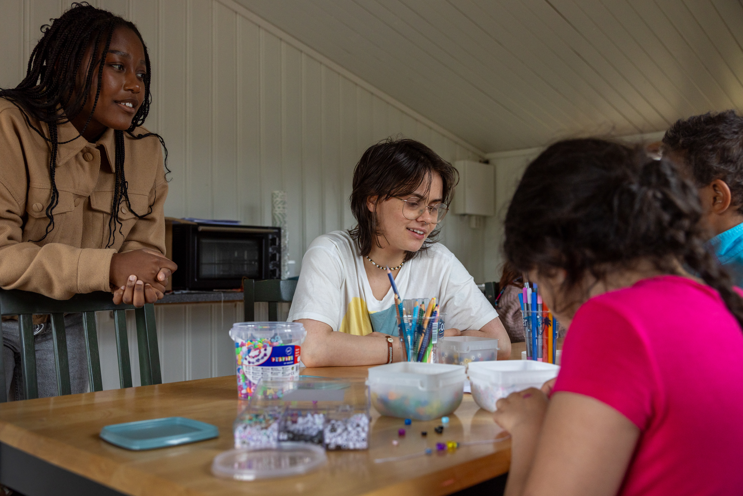 To foto: Det første viser to tenåringsjenter sammen med barn som perler. Det neste bildet viser et ferdig armbånd der det står MAMMA.