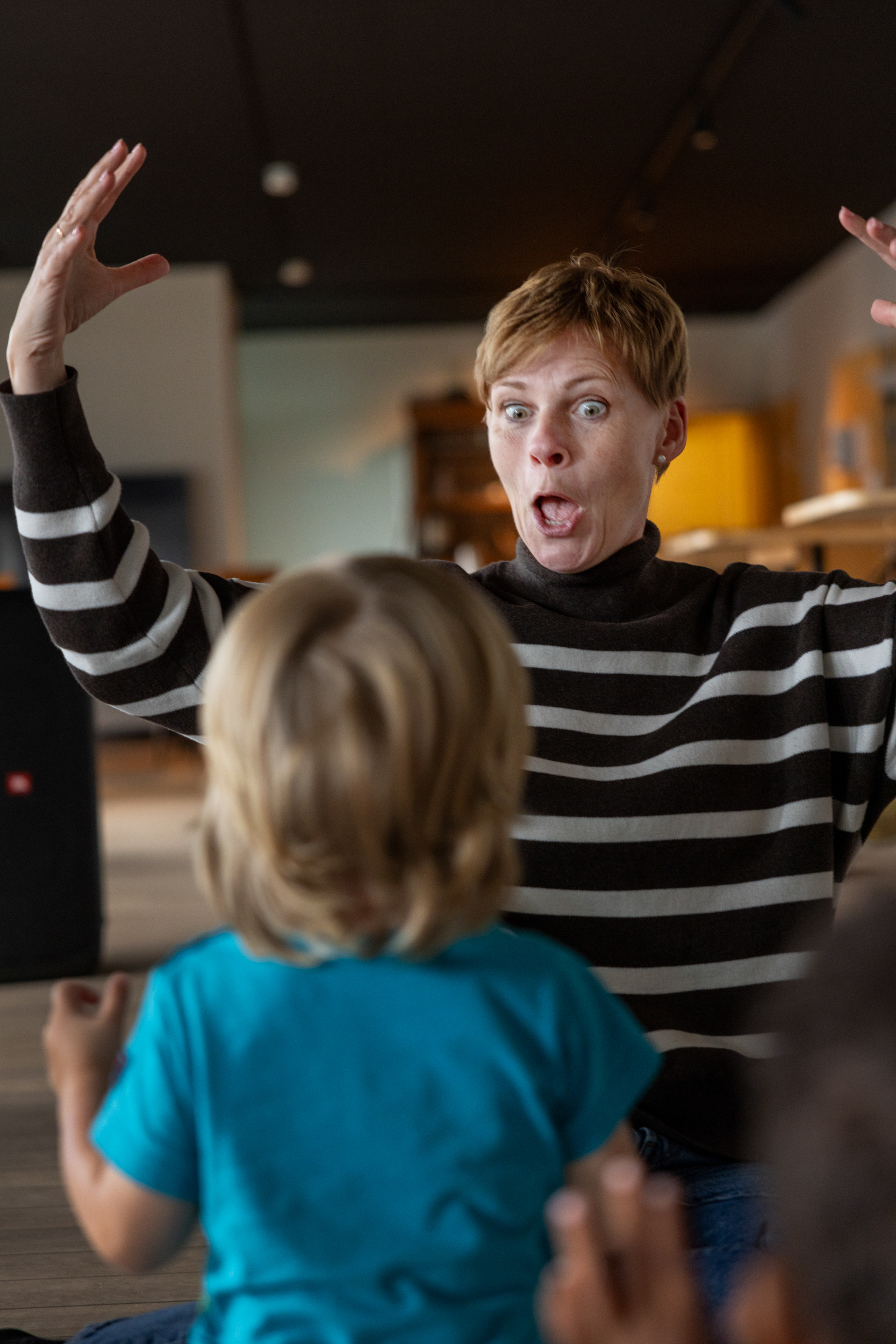 Foto: Voksen kvinne foran et barn inne i et stort lekerom. Hun holder opp armene og gjør grimaser.