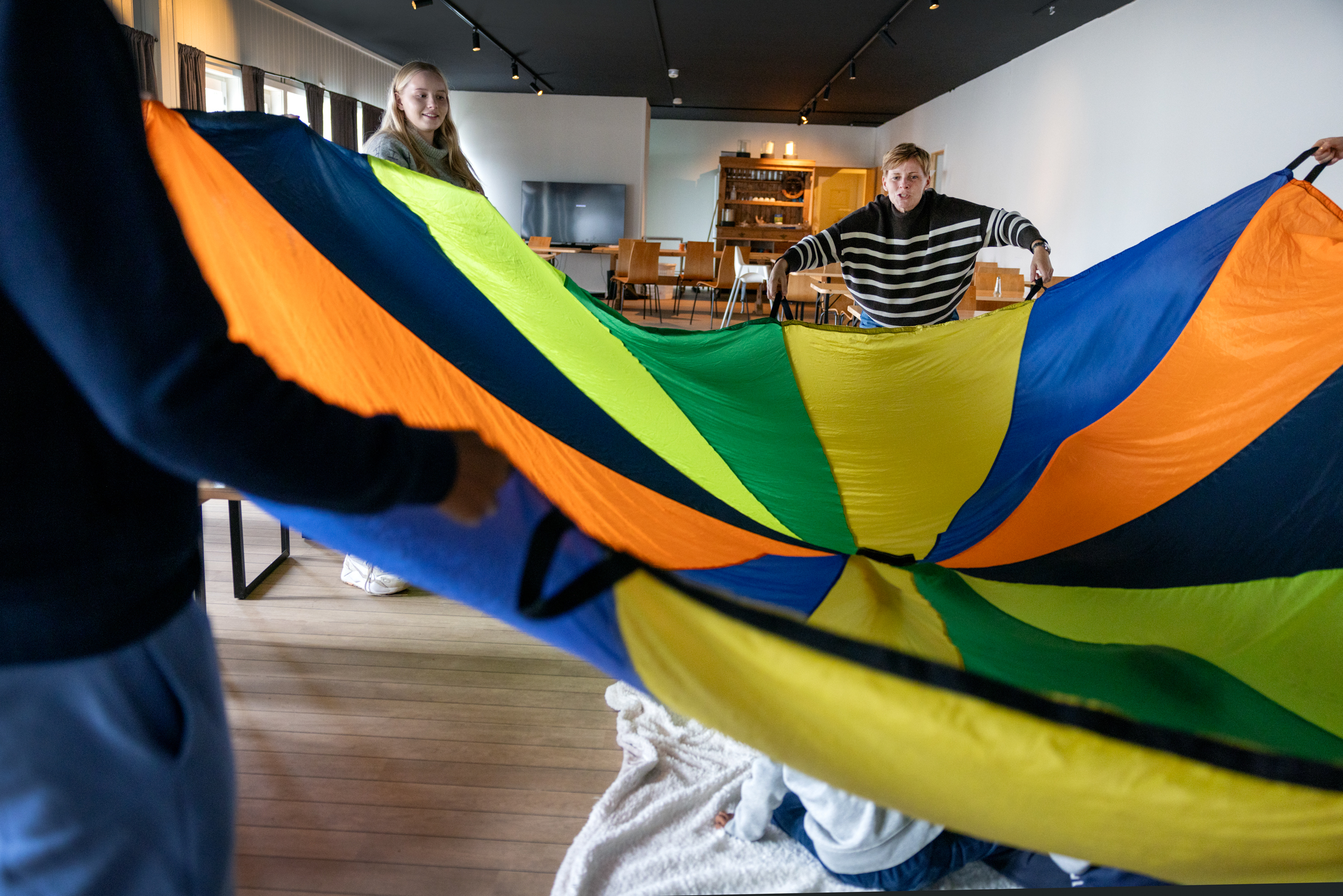 To foto: Første viser en tenåring som blåser såpebobler på noen barn som sitter inne i en lekestue. Det andre bildet viser en stor, fargerik seilduk som voksne holder i og som de hever og senker over barna som sitter på gulvet.