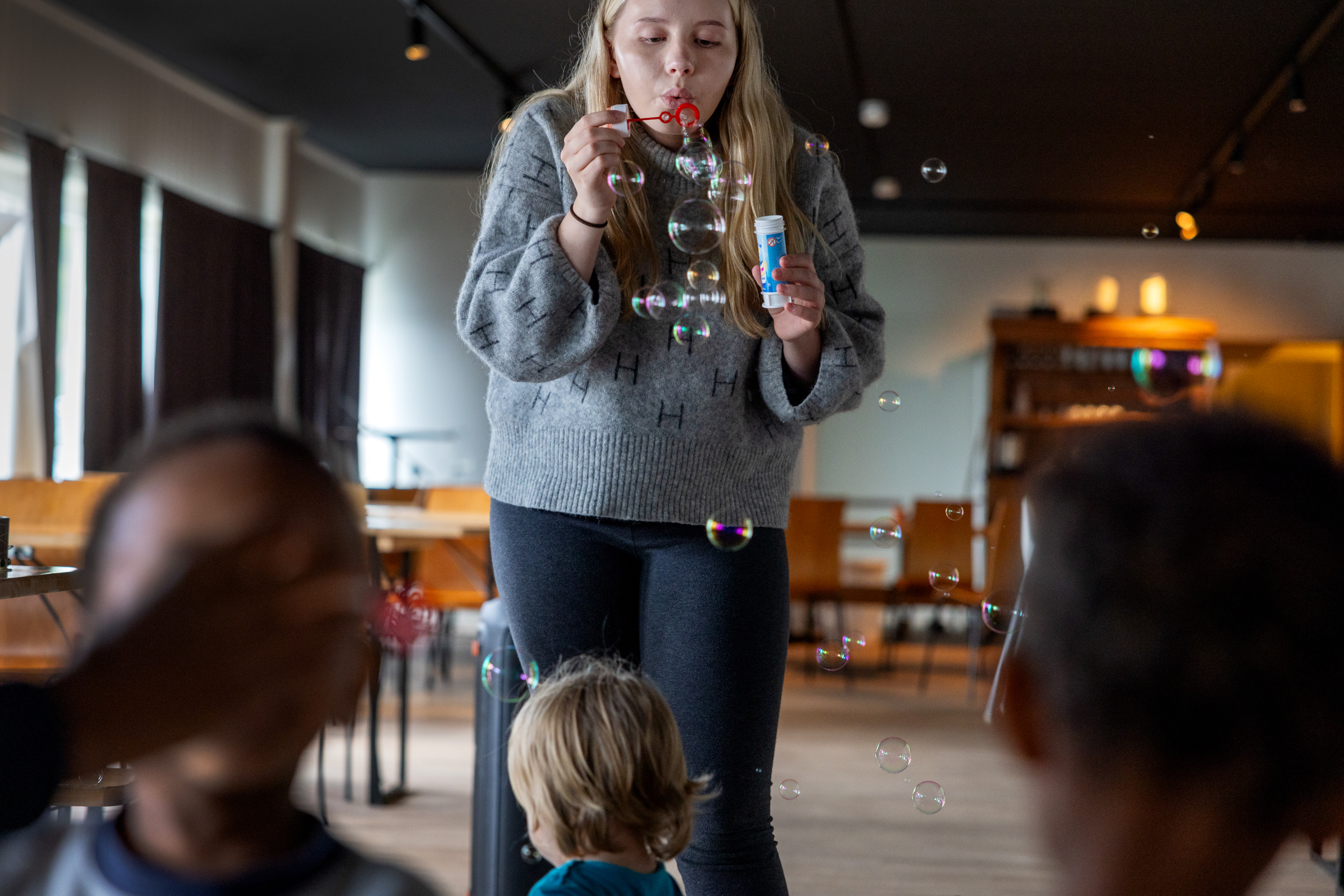 To foto: Første viser en tenåring som blåser såpebobler på noen barn som sitter inne i en lekestue. Det andre bildet viser en stor, fargerik seilduk som voksne holder i og som de hever og senker over barna som sitter på gulvet.