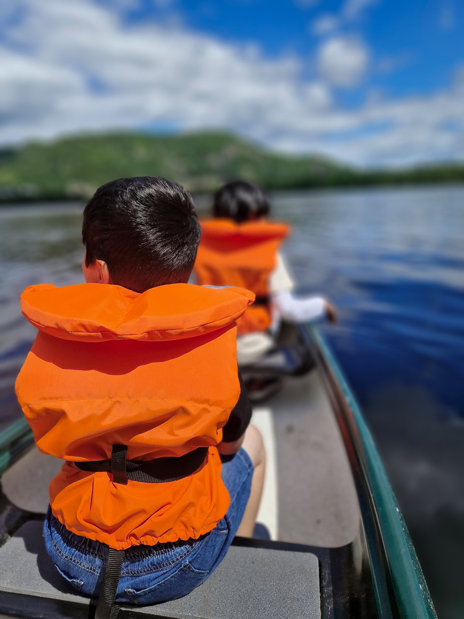 Foto: To barn i oransje redningsvester i grønn kano ute på sjøen. De sitter med ryggen til fotografen.