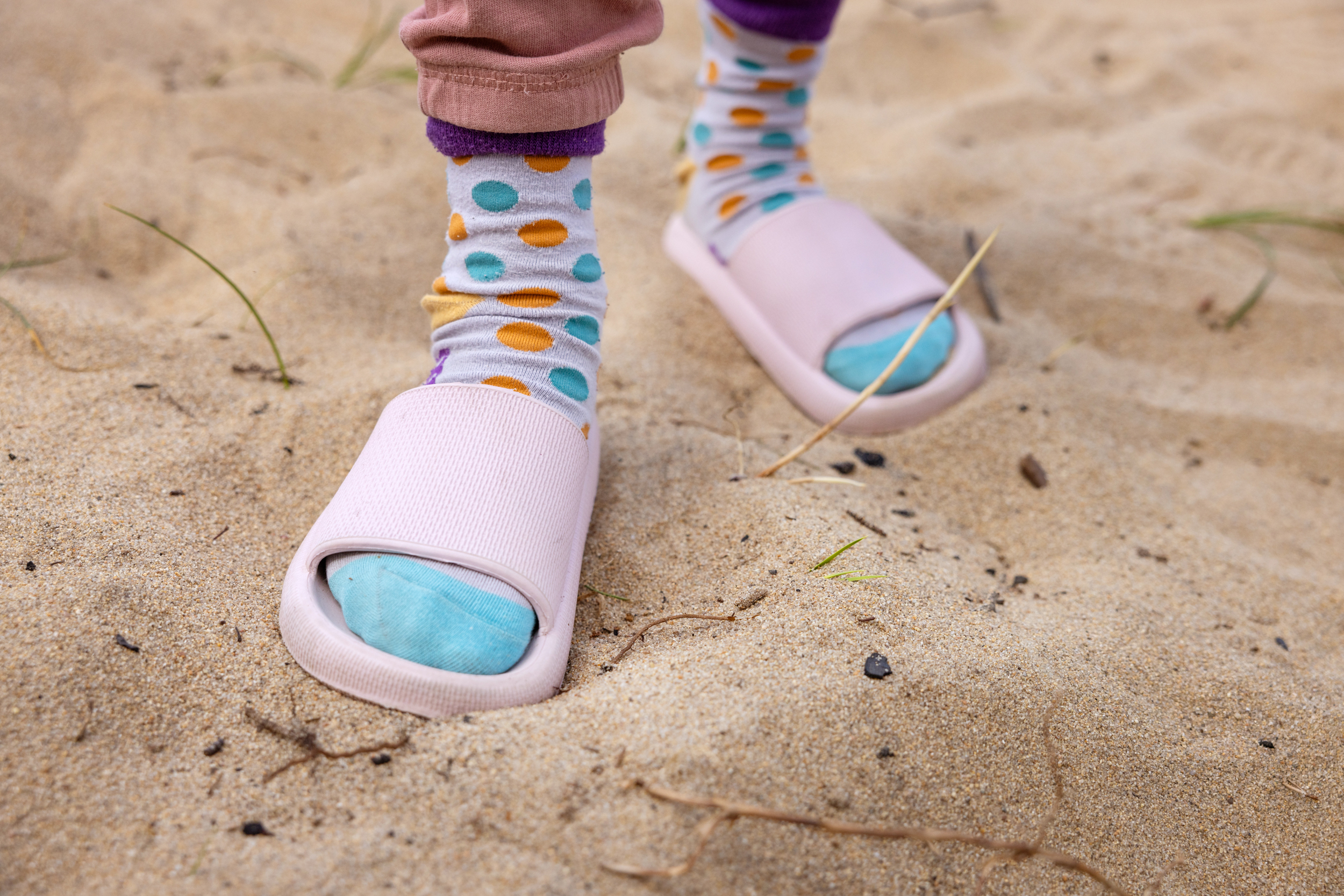 To foto: Først ei jente i småskolealder som slår hjul i sanden like ved sjøen. Deretter nærbilde av de prikkete strømpene hennes i rosa strandtøfler.