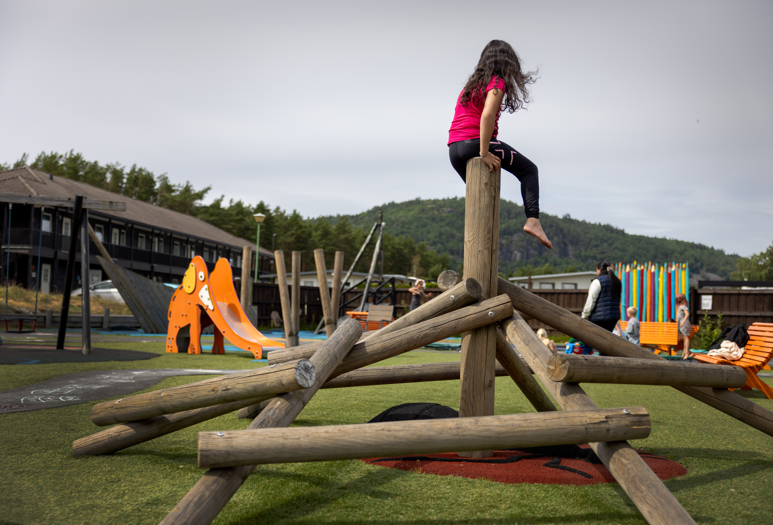 Foto: Jente sitter på toppen av et klatrestativ på lekeplassen.