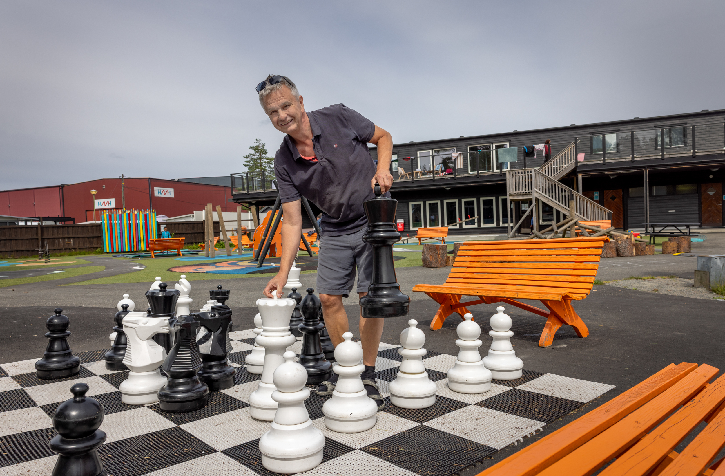 Foto: Mann i 60-årene som flytter på kjempestore sjakkbrikker utendørs.