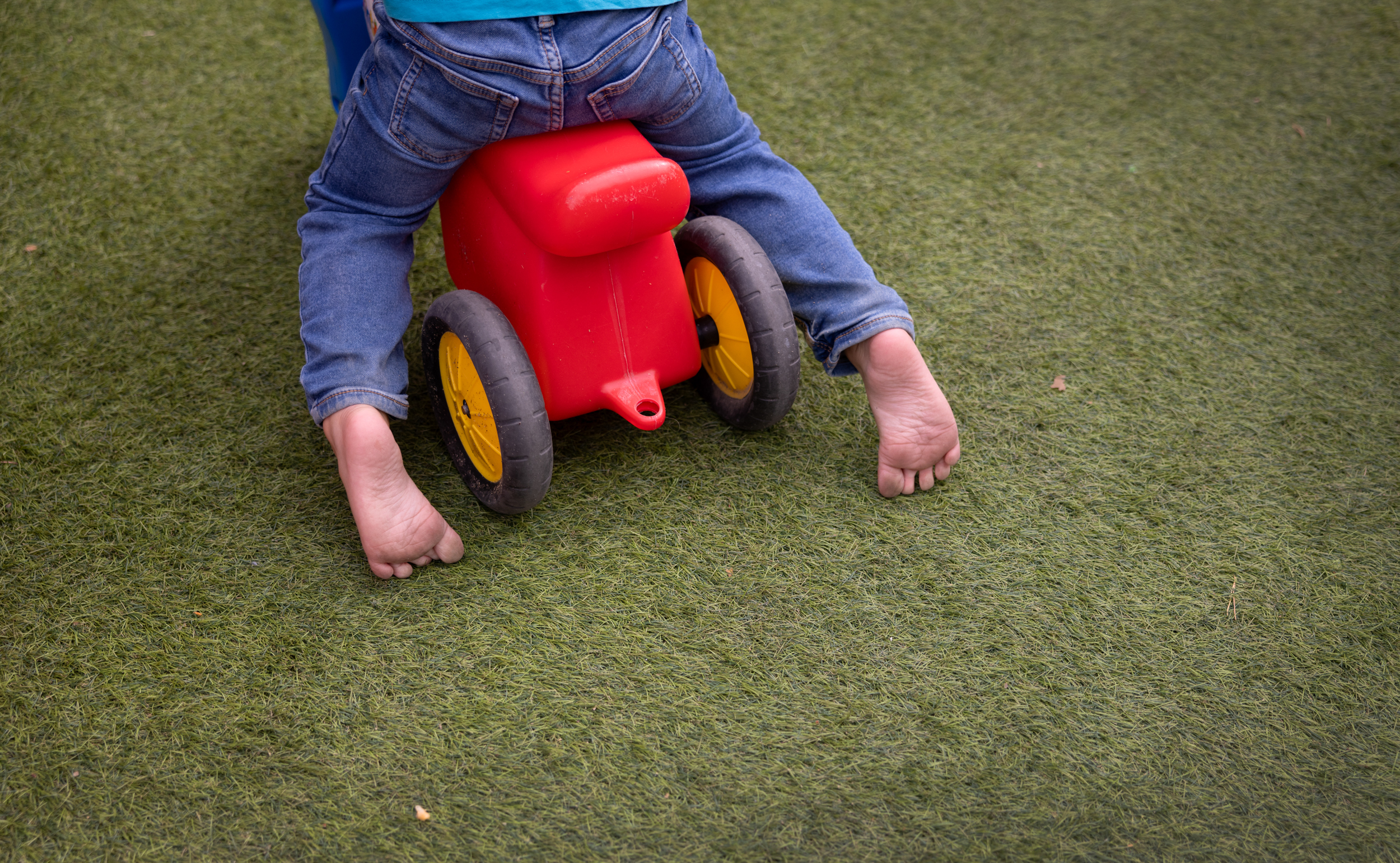 Foto: Lår, legger og føtter til en 3-åring som sparker seg av gårde på en liten plastbil.