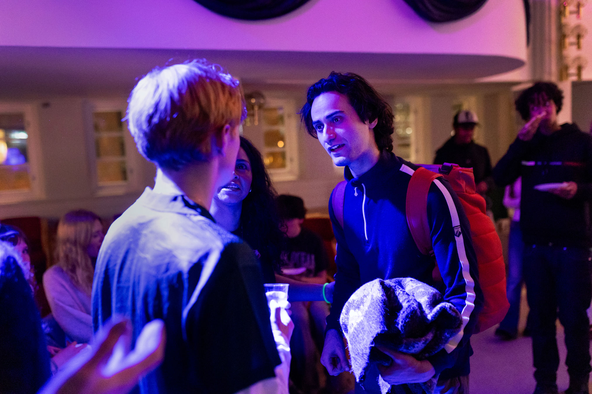 Foto: I blålilla lys står to unge menn og snakker sammen.
