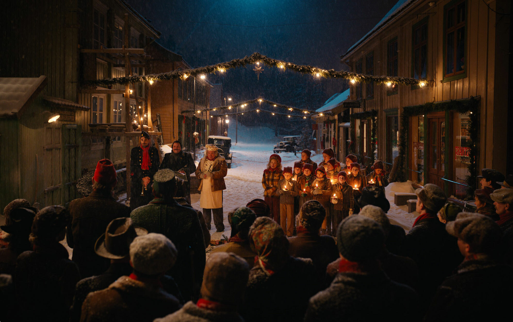 Barnekor med tente lykter og en rekke andre menensker står samlet på torget i mørket. Julestemning.