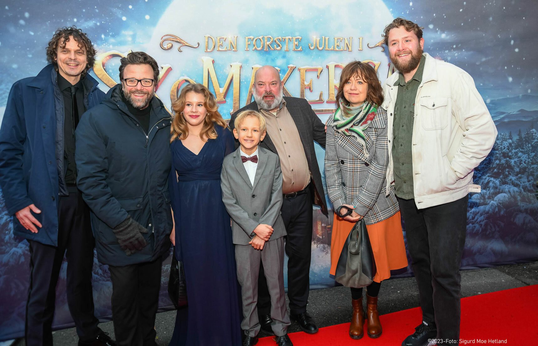 To barn og fem voksne står foran filmplakaten til den nye filmen om skomakergata. Dette er regissøren sammen med skuespillerne.