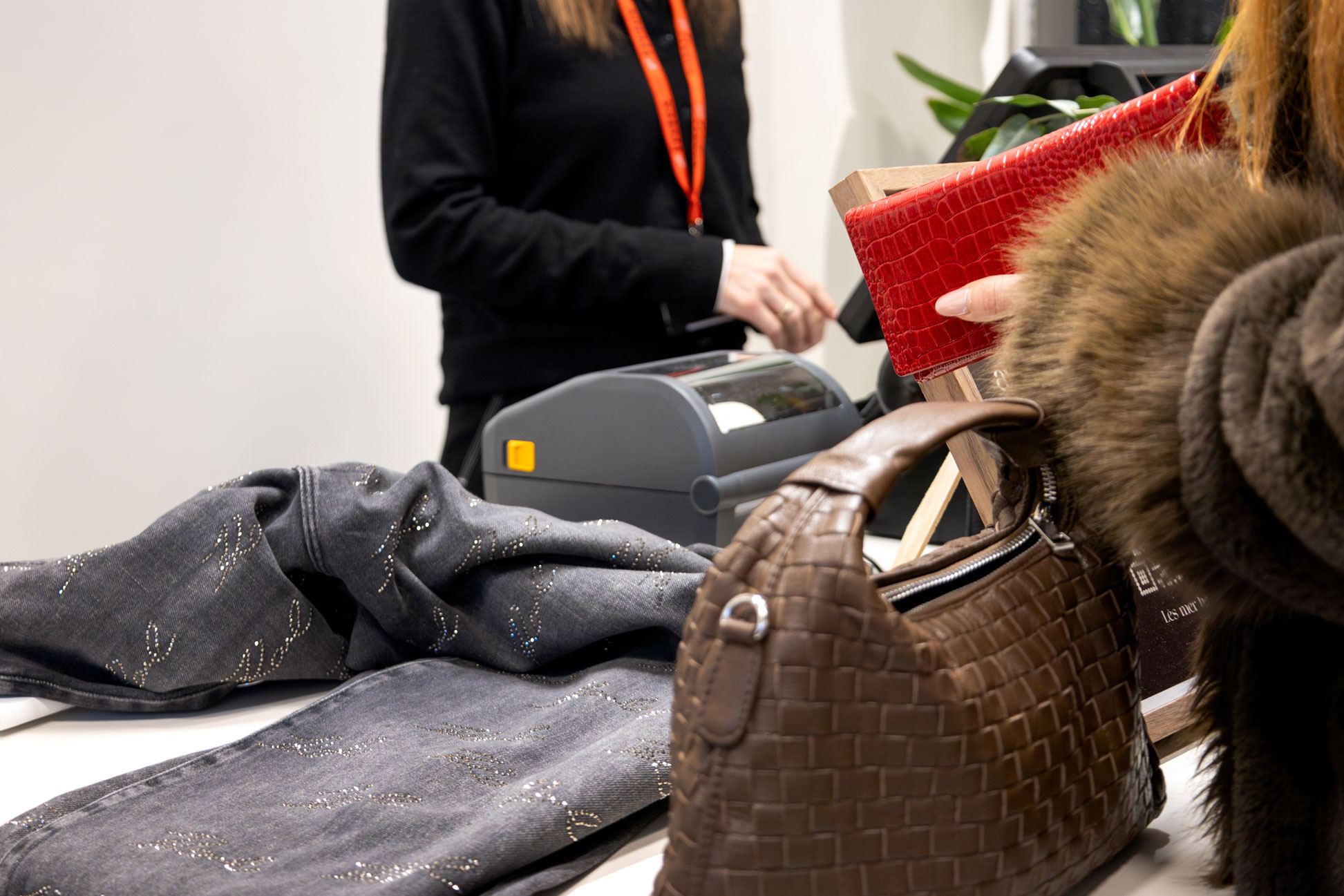 Foto: Varekjøp i klesbutikk der det ligger en svart bukse med glitter på disken. Det står en dame bak kassen og en annen dame holder en lommebok som hun har tatt ut av en brun veske. Vi ser ikke hodene til noen av damene.