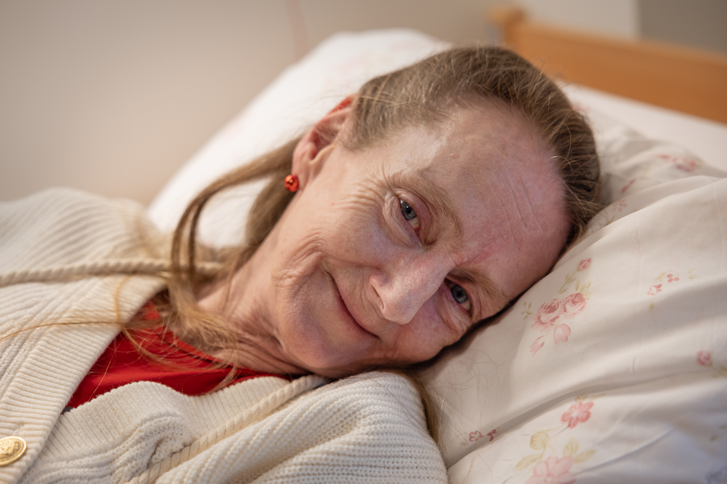 Foto: Kvinne med langt, blondt hår smiler fra sykesengen.