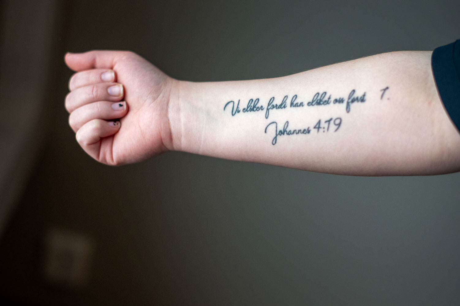 Foto: Av hvit underarm der det er tatovert inn tekst med løkkeskrift. Den er hentet fra Bibelen.