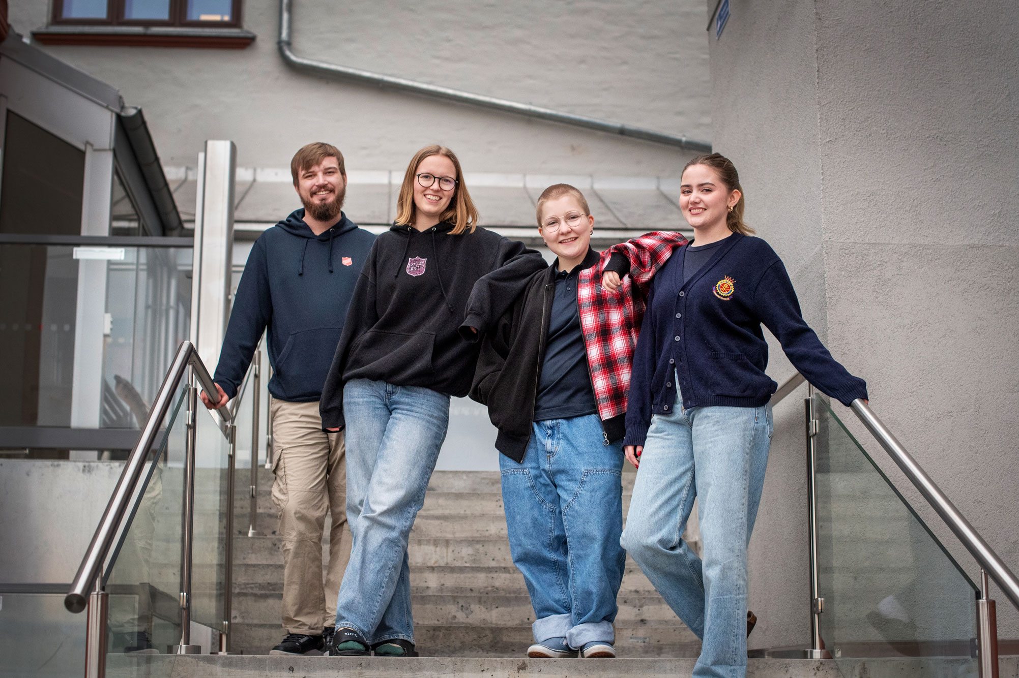 Foto: En ung mann med skjegg og fire unge jenter står sammen i en trapp. De har på seg hverdagslige klær og ellers logo fra Frelsesarmeen.