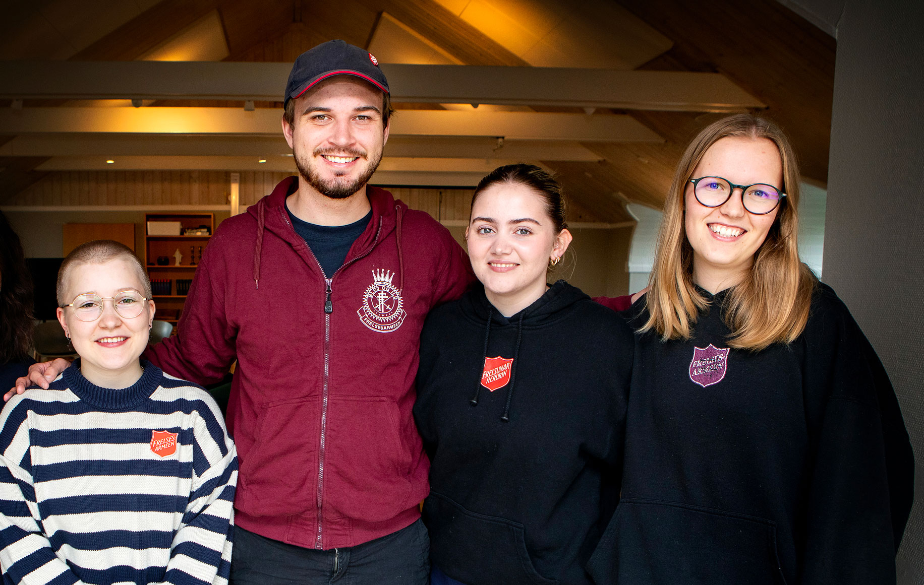 Foto: Gruppebilde inne i en stor loftstue av en mann og tre kvinner. Aller i 20-årene.