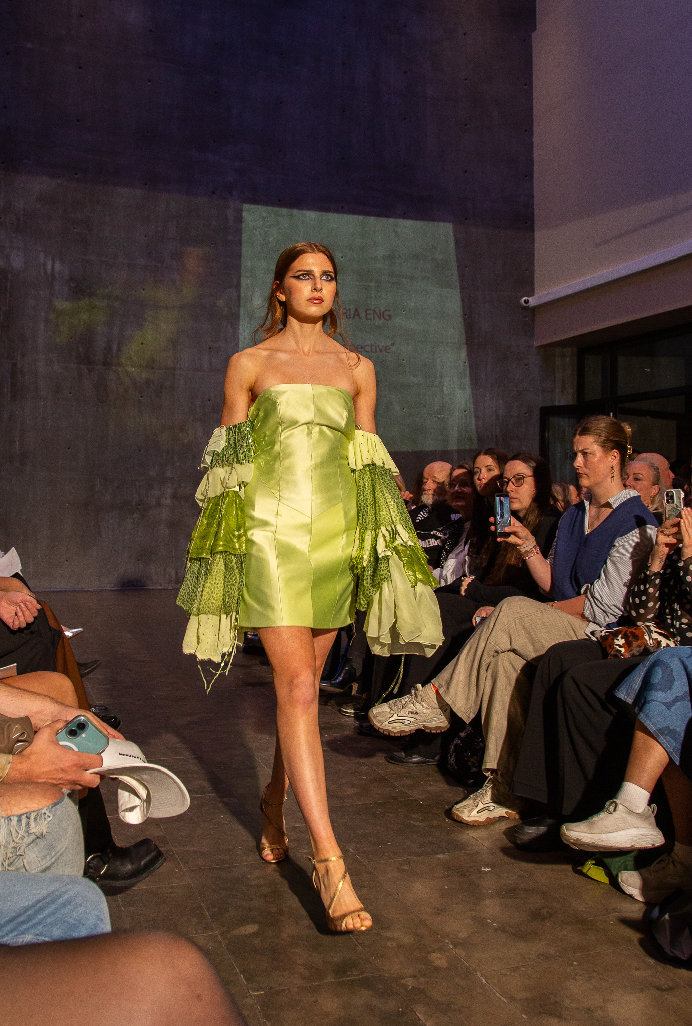 Ung modell går på catwalk i grønn håndsydd kjole.