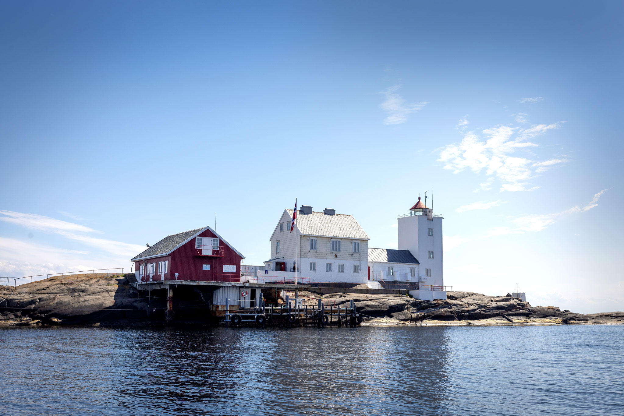 Foto: Blå himmel og noen gamle bygninger på en liten holme med fyrlys.