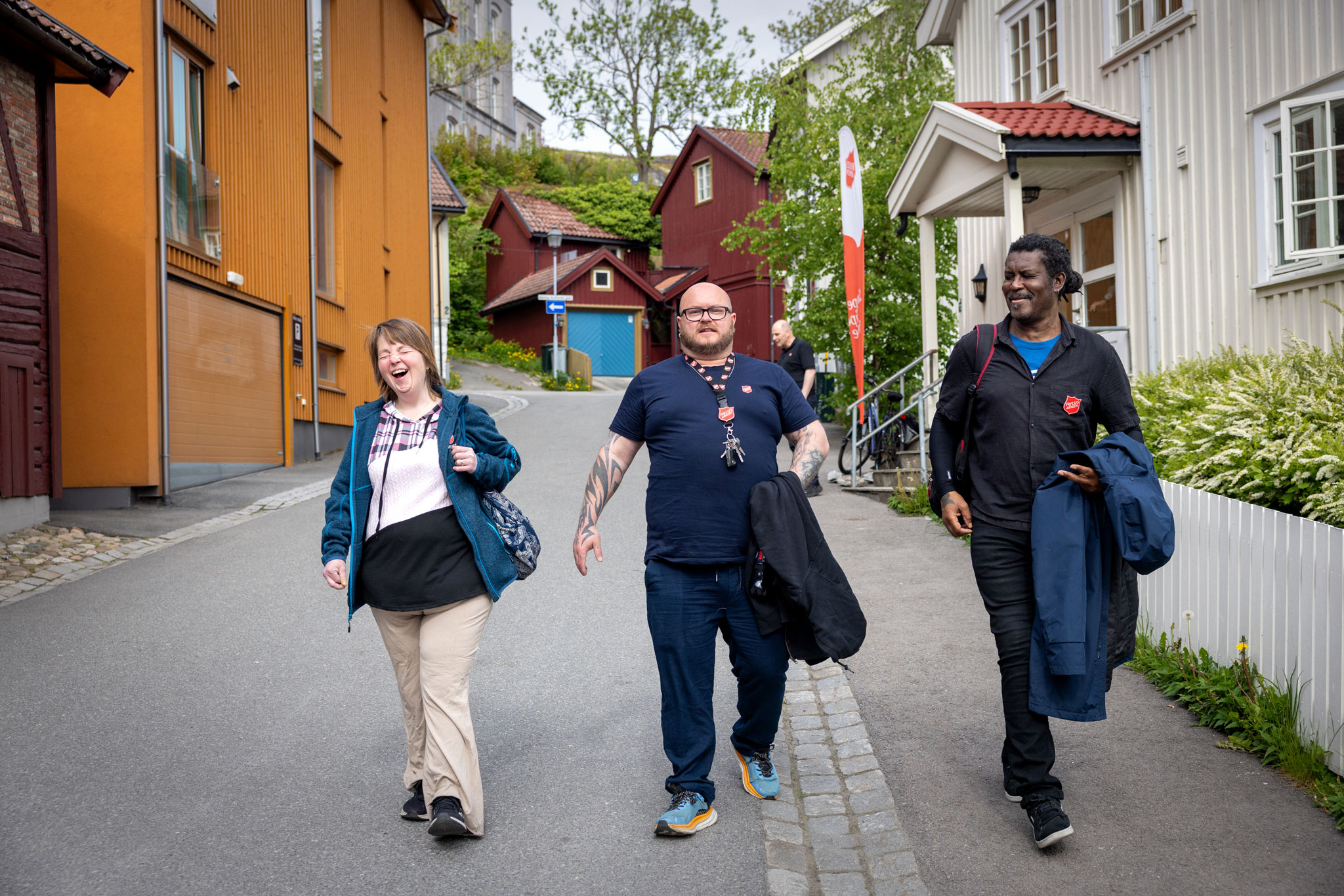 Foto: En kvinne og to menn går nedover en asfaltert gate med gamle hus på begge sider.