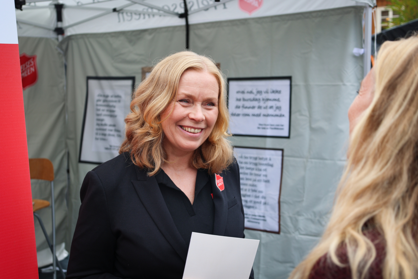 Frelsesarmeesoldat i blå uniform foran et eventtelt. Hun smiler mot en annen kvinne.