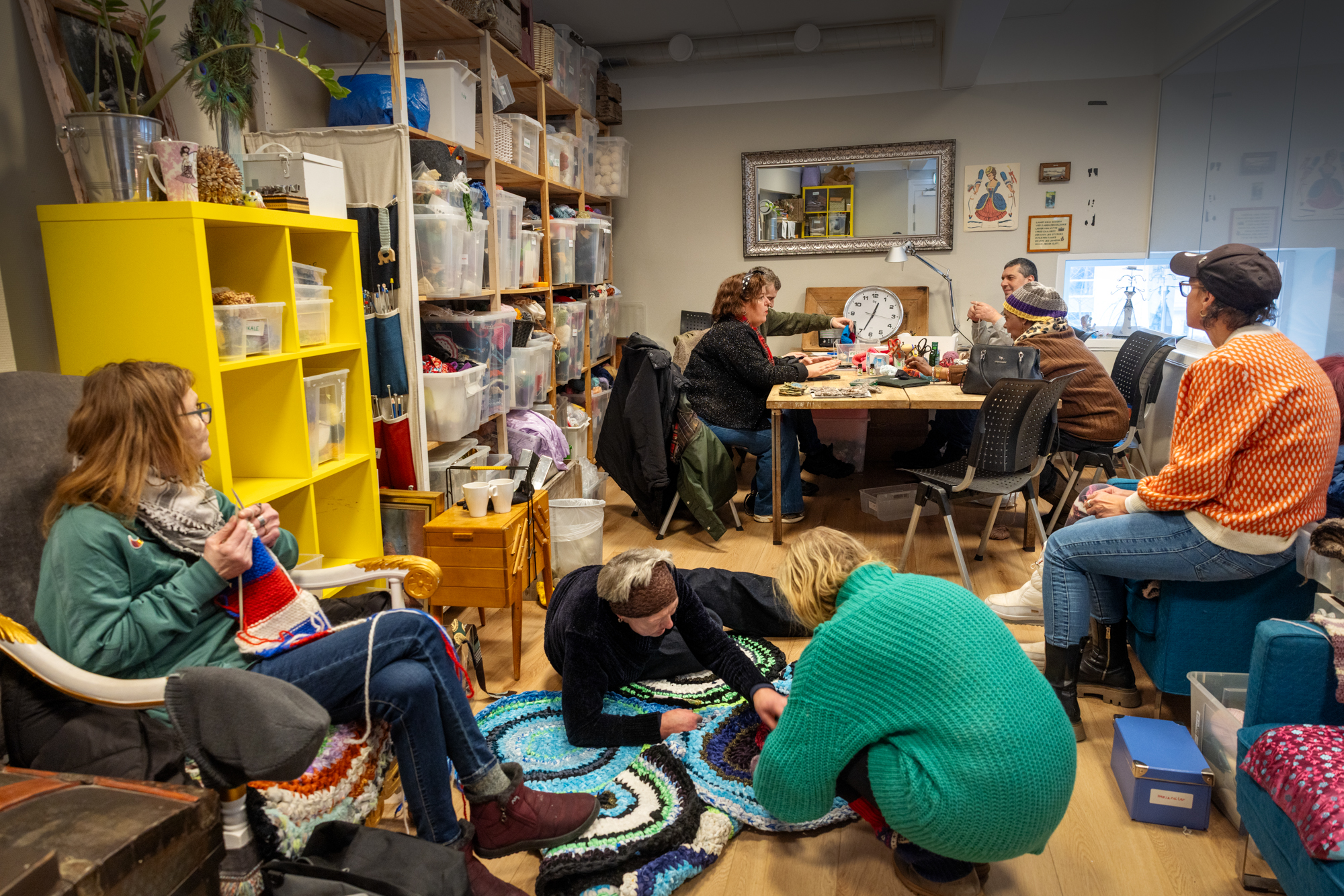 Foto: Hobbyrom med 7-8 personer i. Alle er opptatt med å lage ulike ting. Den er en rekke hyller langs veggen.
