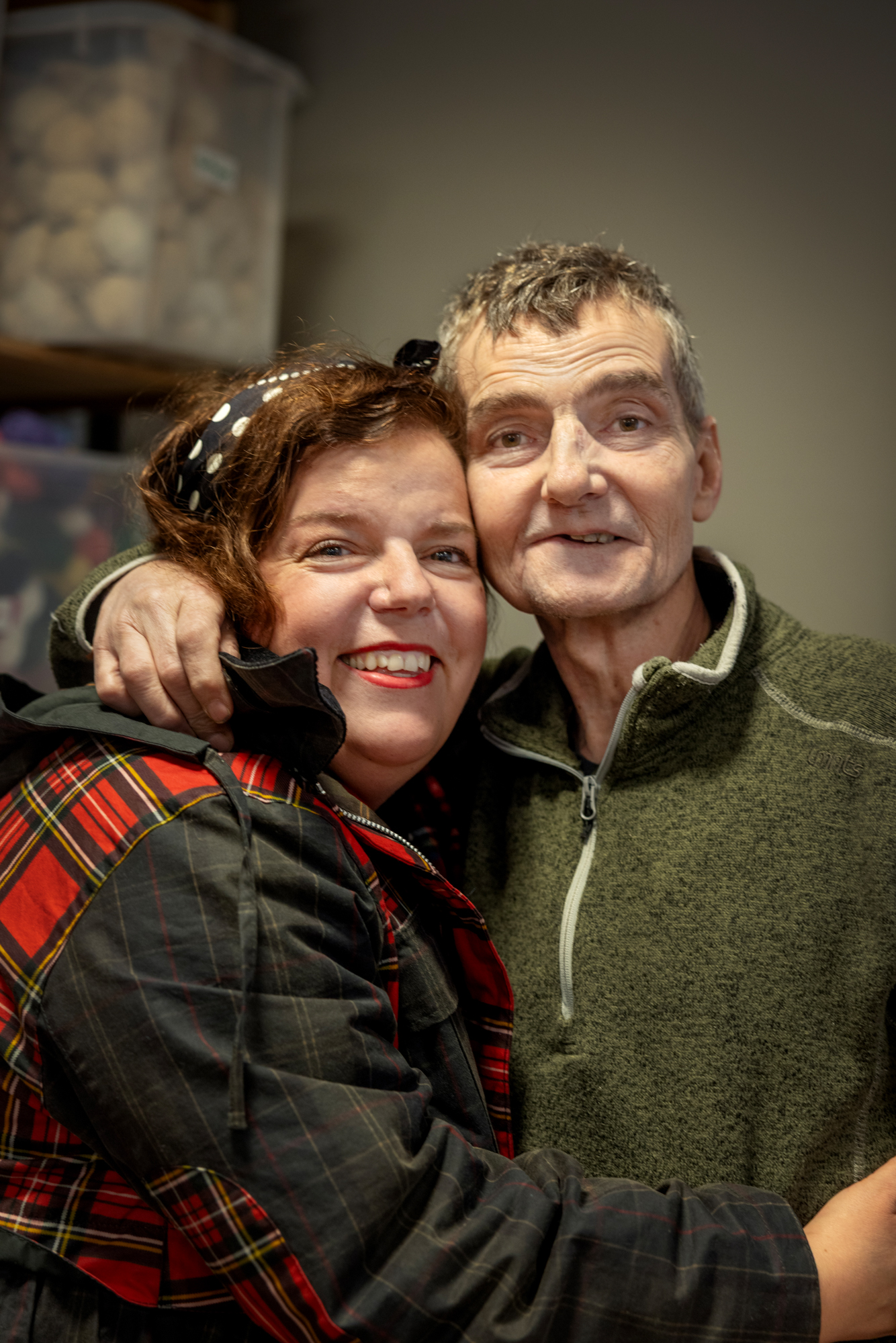 Foto: Mann i grønn fleece holder armen rundt en kvinne med mørkt hår. Hun har på seg en grønn jakke med rødrutete detaljer. Hun smiler.