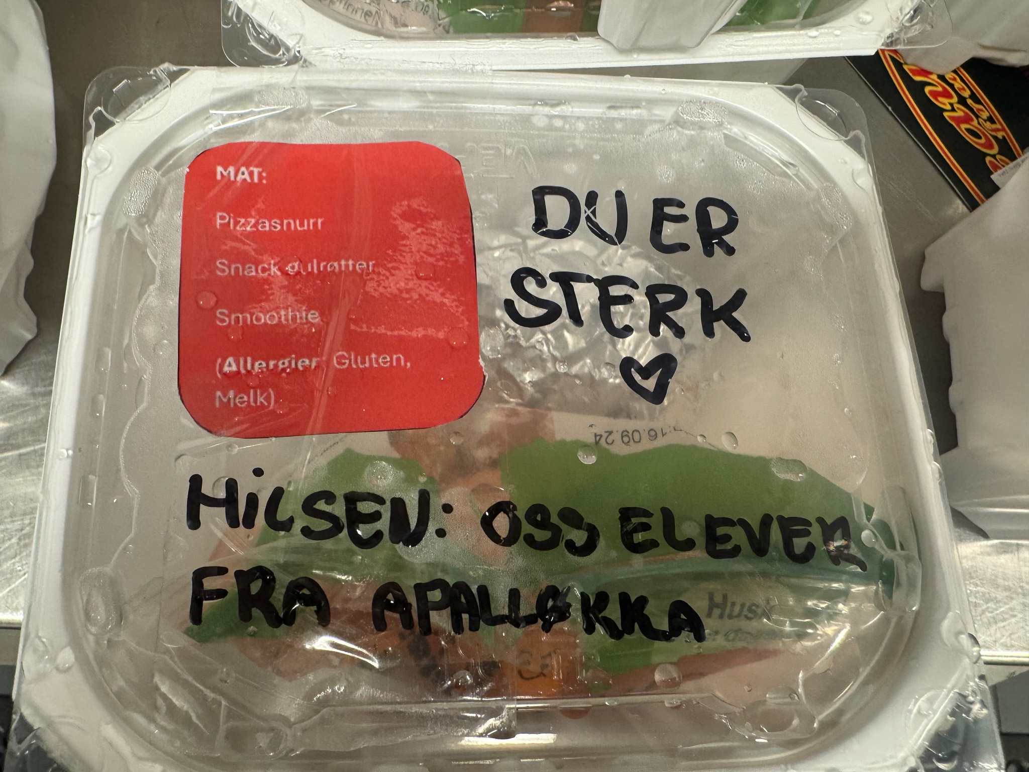 Foto: Matpakke i et beger med plastlokk. Noen har skrevet inn teksten: Du er sterk. Hilsen: Oss elever fra Apalløkka.