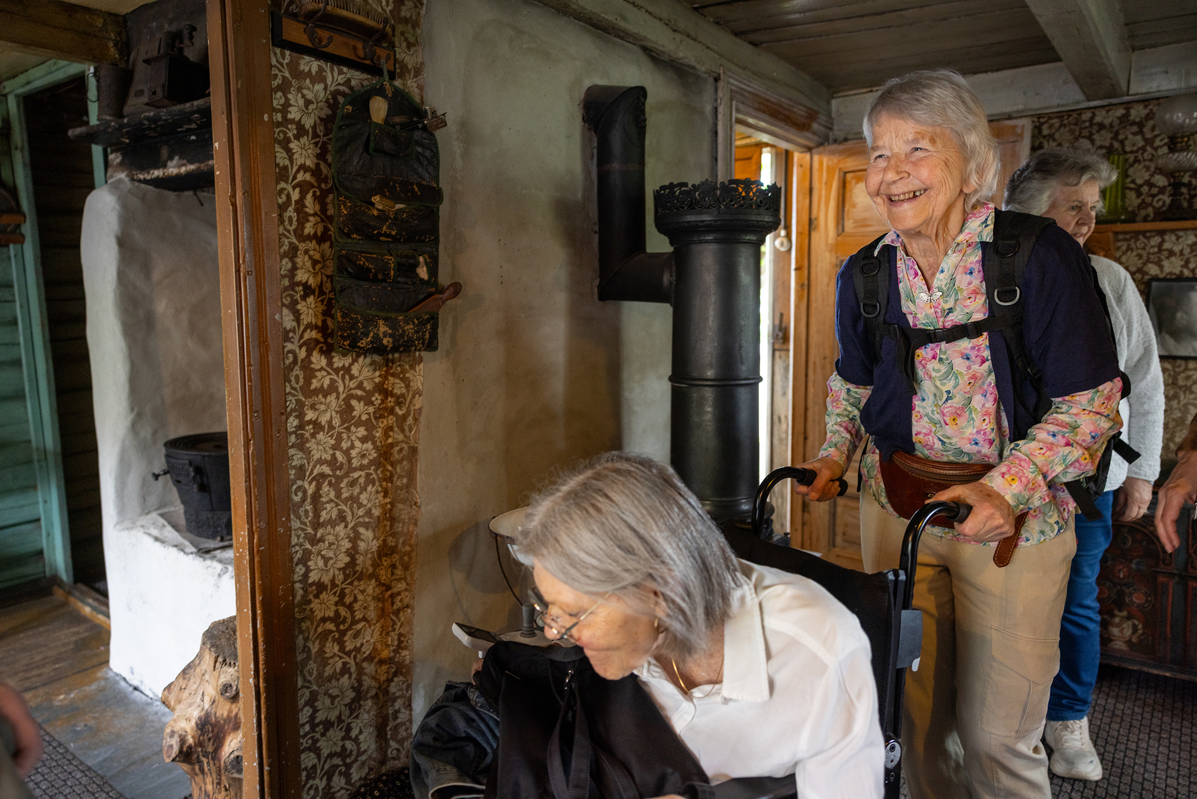 Foto: Eldre kvinne triller eldre en annen eldre kvinne i rullestol inne i et gammelt hus.