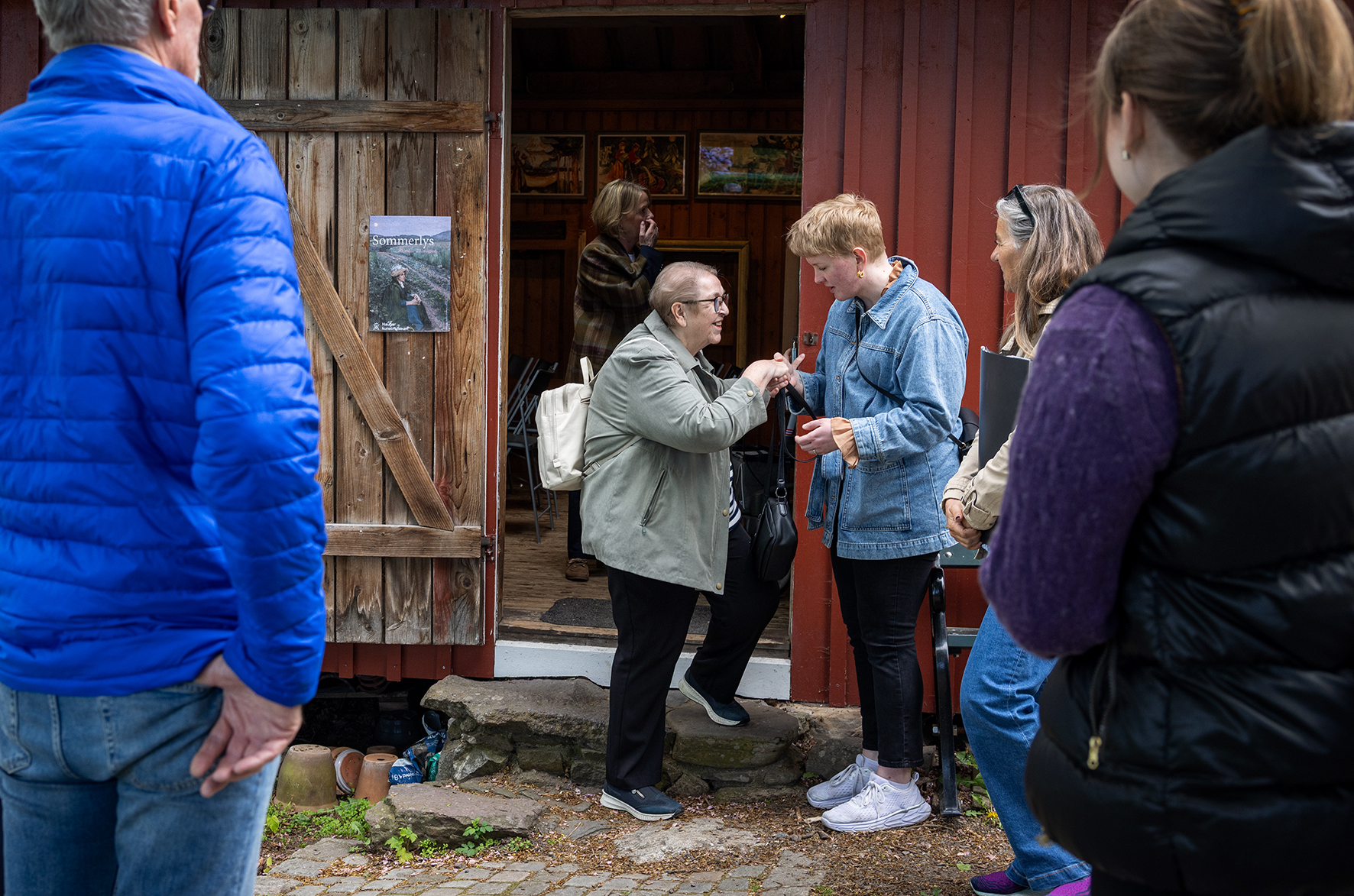 Foto: Flere eldre mennesker står utenfor et lite uthus og diskuterer ivrig.