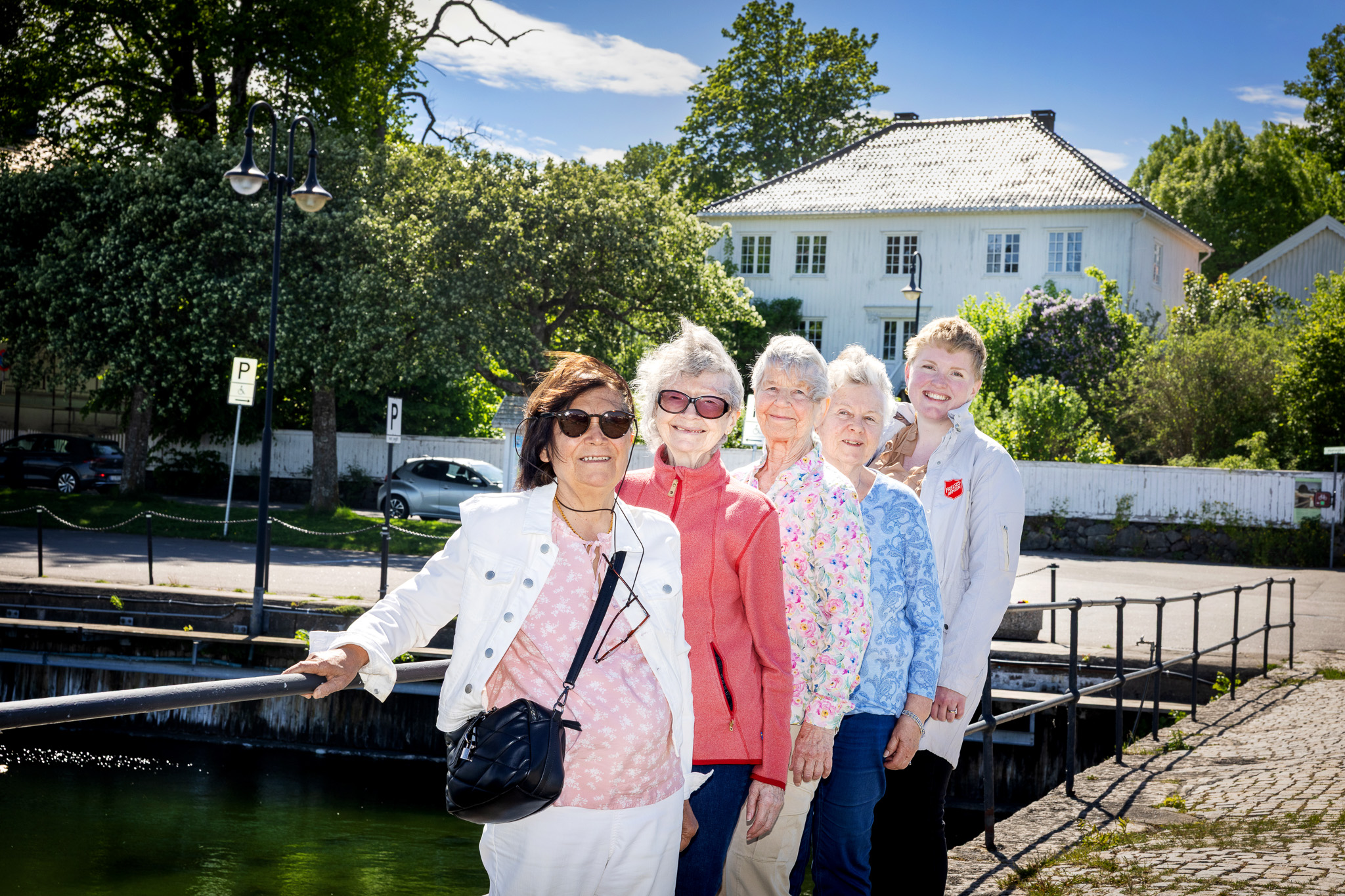 Elde kvinner på rekke og rad på en bro i Åsgårdstrand. Hvitt gammelt hus i bakgrunnen.