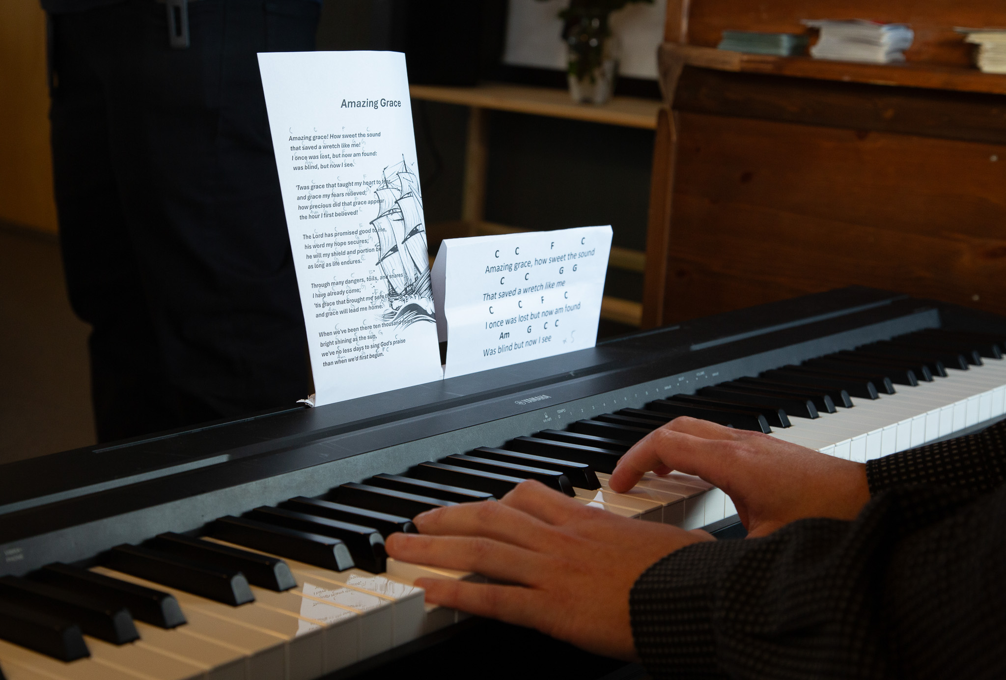 Foto: To hender som spiller på et sort keyboard innendørs. Et papir med tekst og akkorder til sangen Amazing Grace