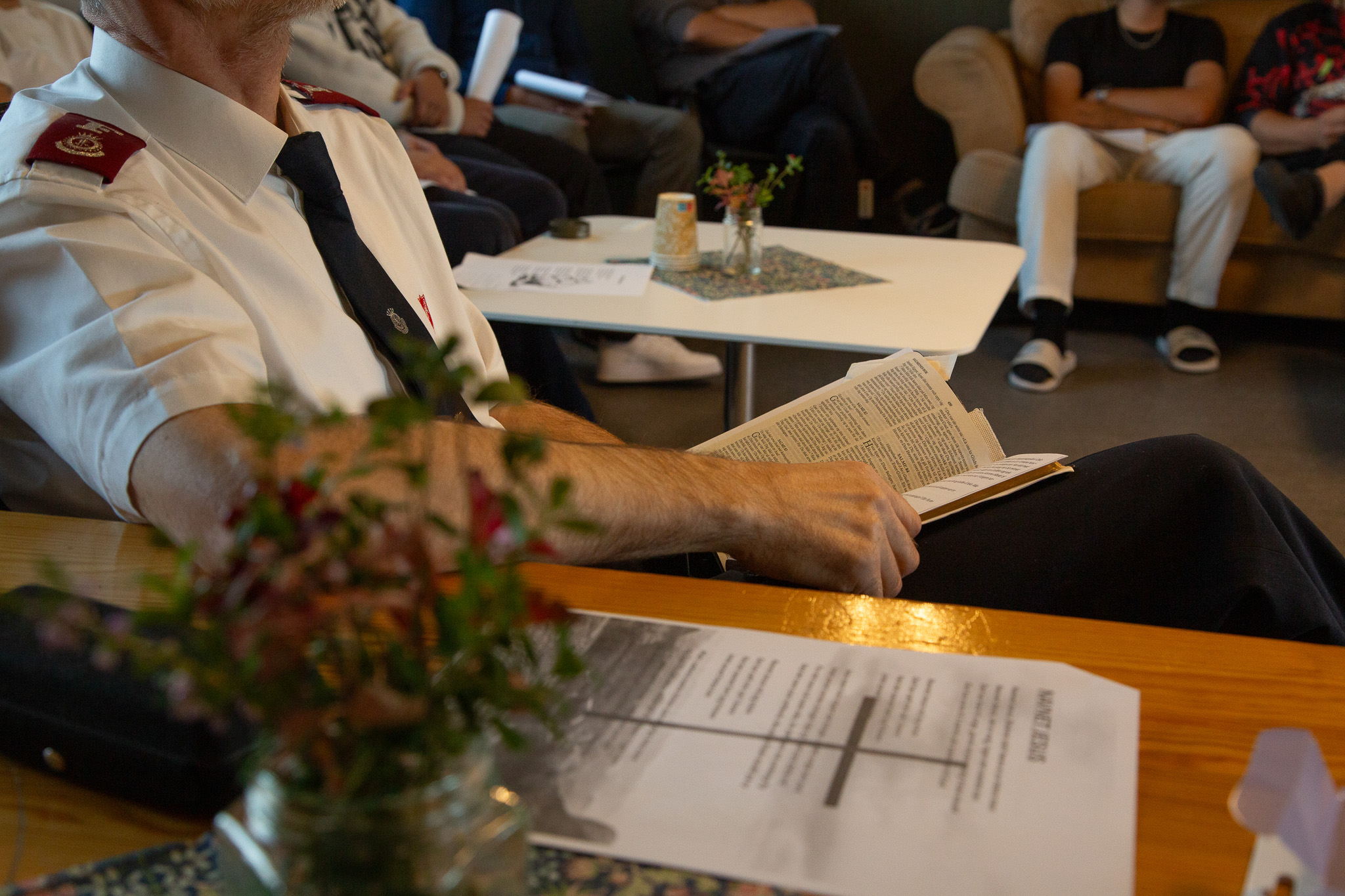 Sangtekster på et bord, blomster og en mann i uniform sitter med en bibel i hendene