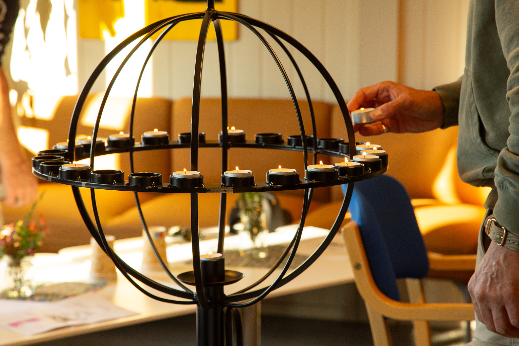 Foto: Inne på et rom legger en mann et tent telys i en lysglobus