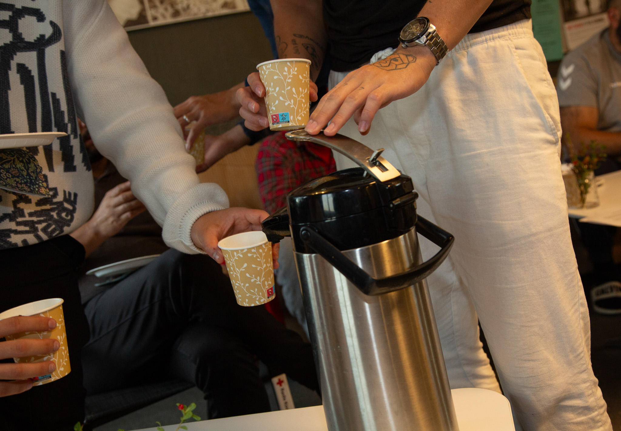 Foto: Flere menn samlet rundt en kaffekanne med pappkrus i hendene.