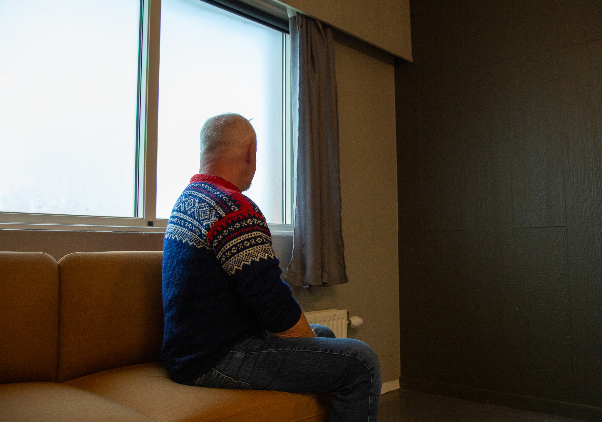 Mann i strikkegenser sitter på en sofa og ser ut av et vindu