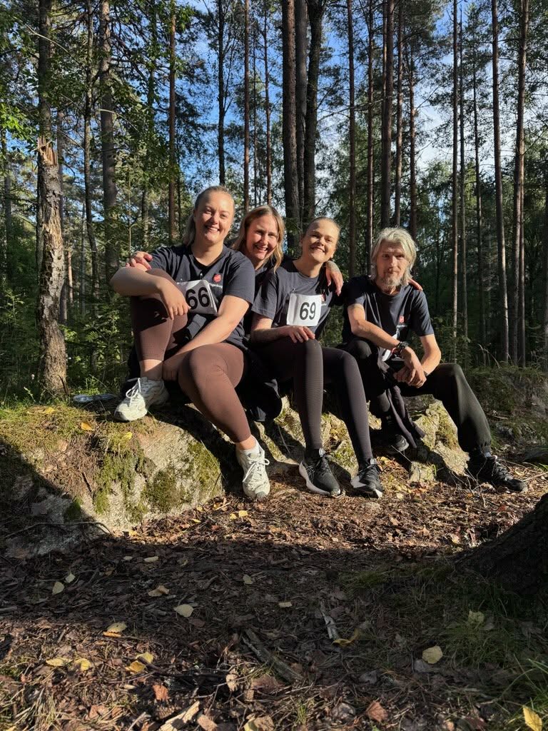 Tre kvinner og en mann sitter i skogen. De har nummerlapp på brystet og treningsklær og joggesko.