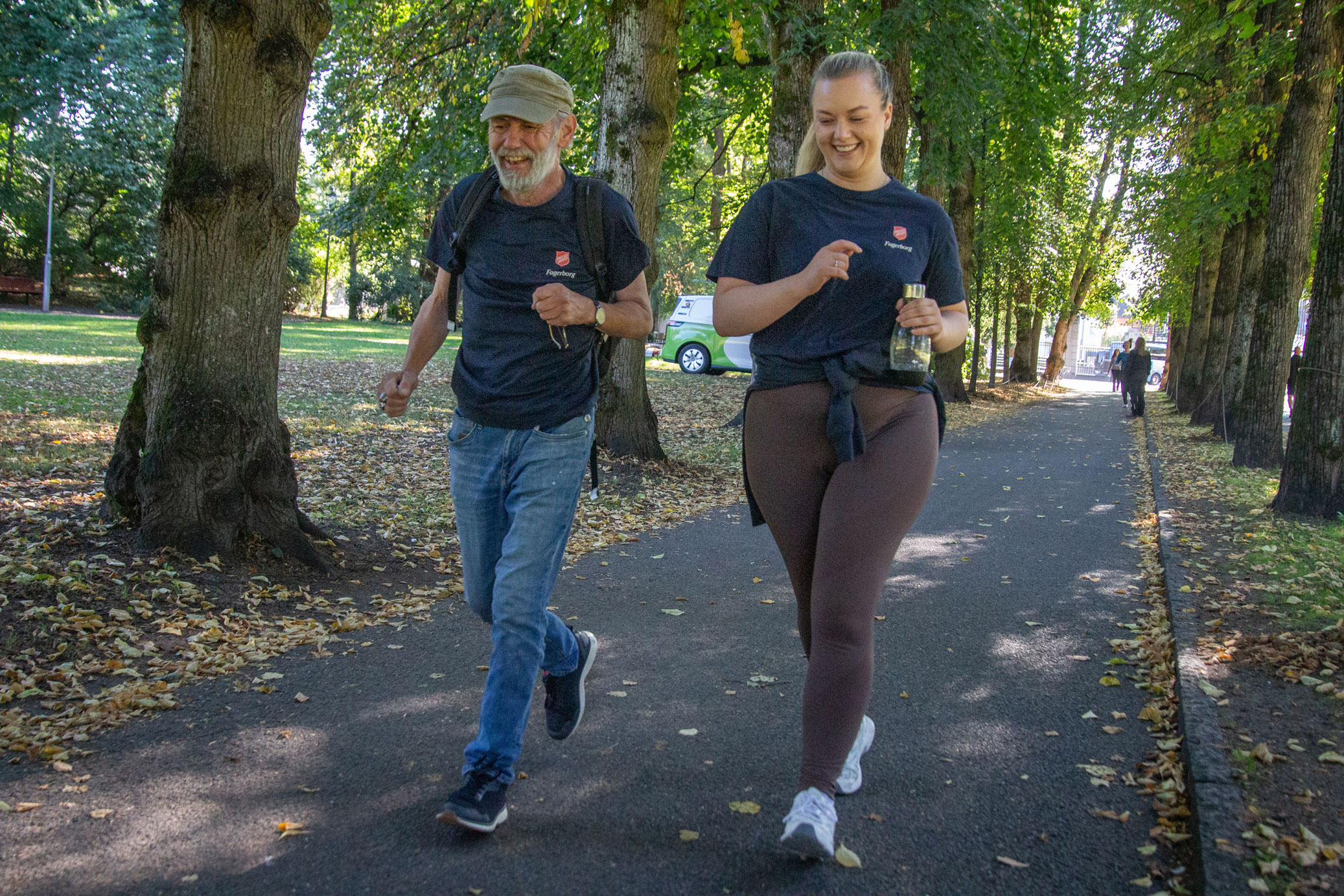 Mann med grått hår og skjegg i 50-årene løper ved siden av en kvinne u 30-årene med blond hestehale. Det har på matchende T-skjorter med Frelsesarmeens logo. Hun har tights og han dongeribukse og sekk på ryggen.
