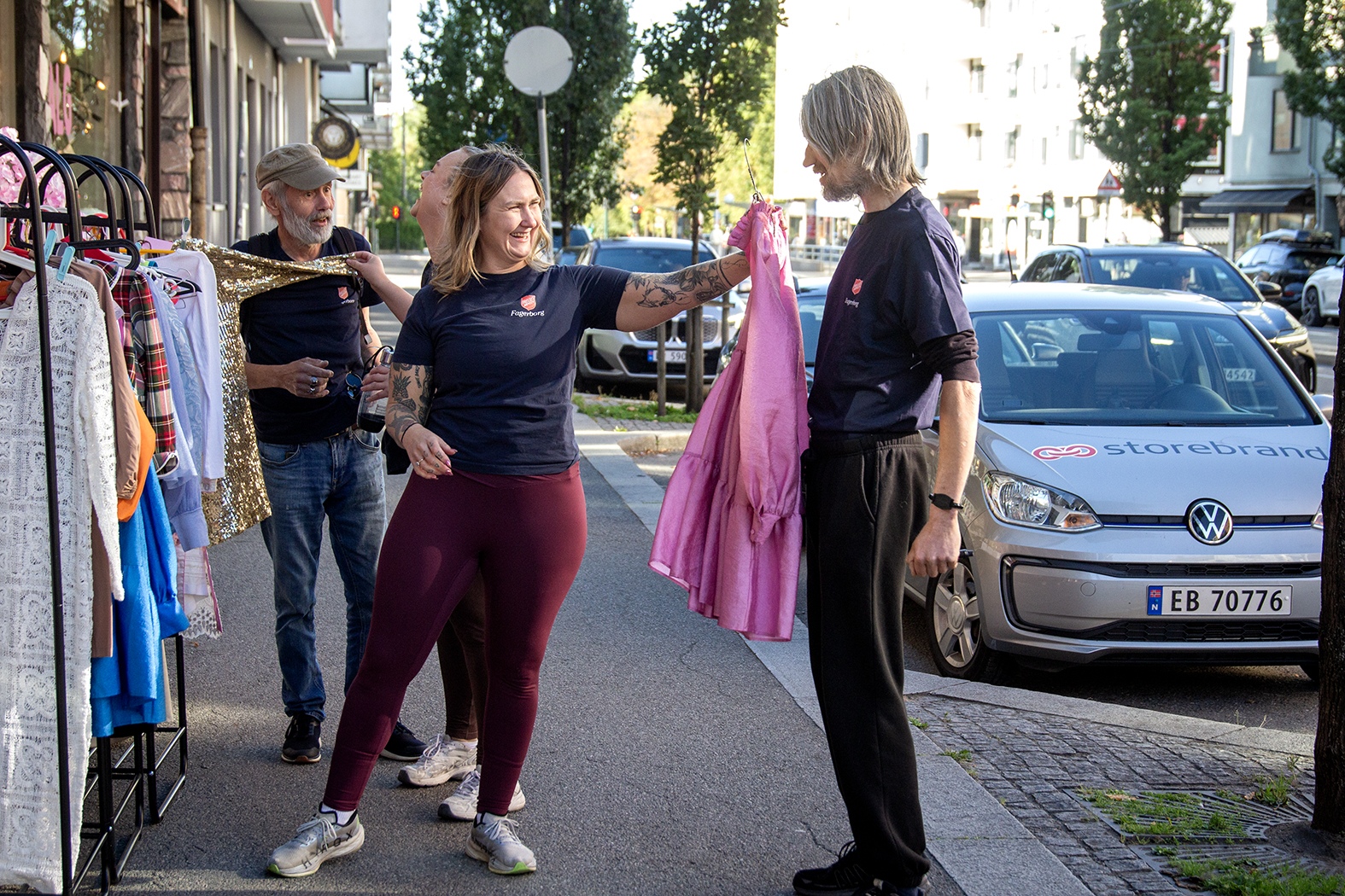 Personer som står på gata ved et stativ med klær. En kvinne holder opp en rosa kjole.