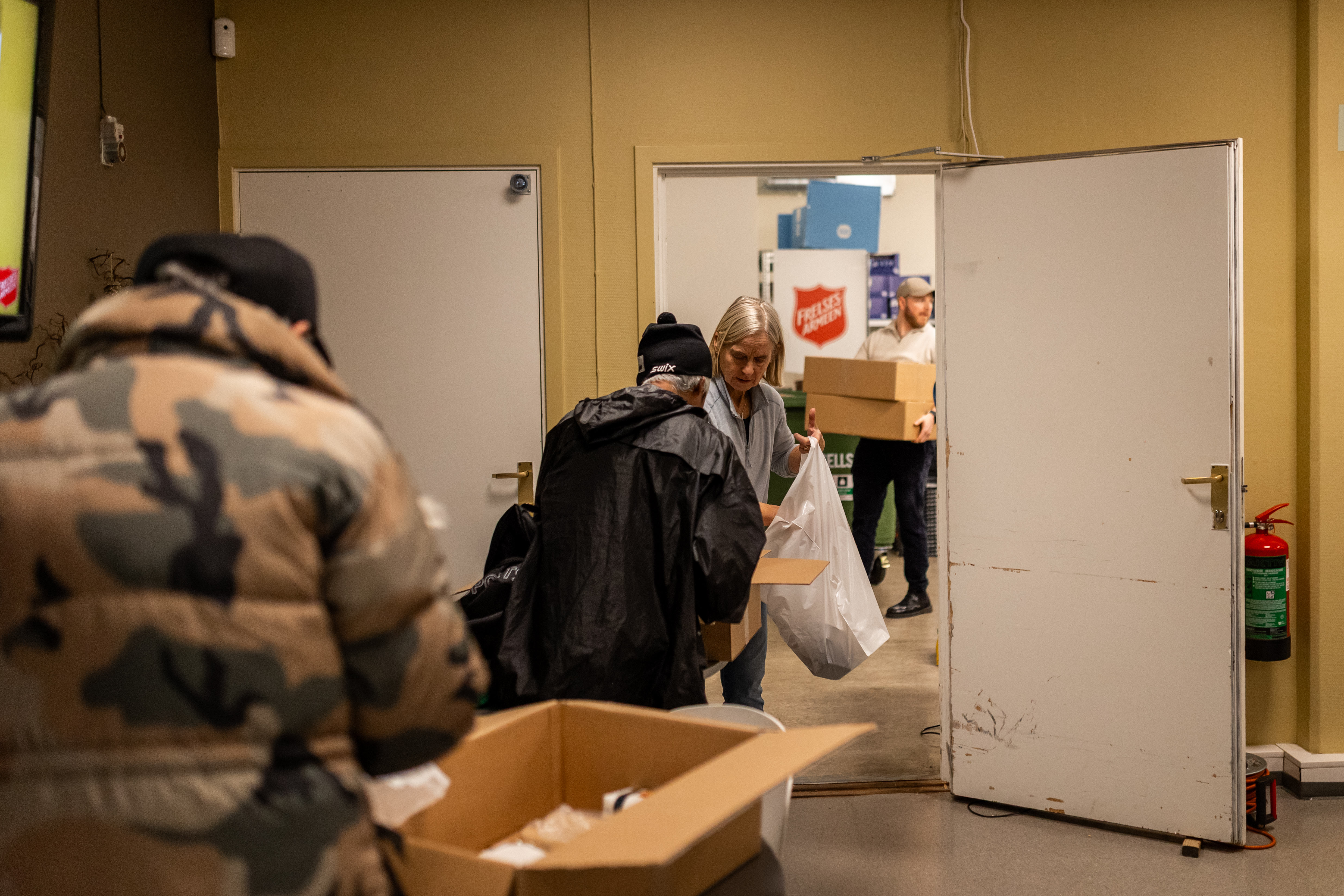 Foto: Fra en matutdeling i et lokale. To menn henter mat hos en dame fra Frelsesarmeen.