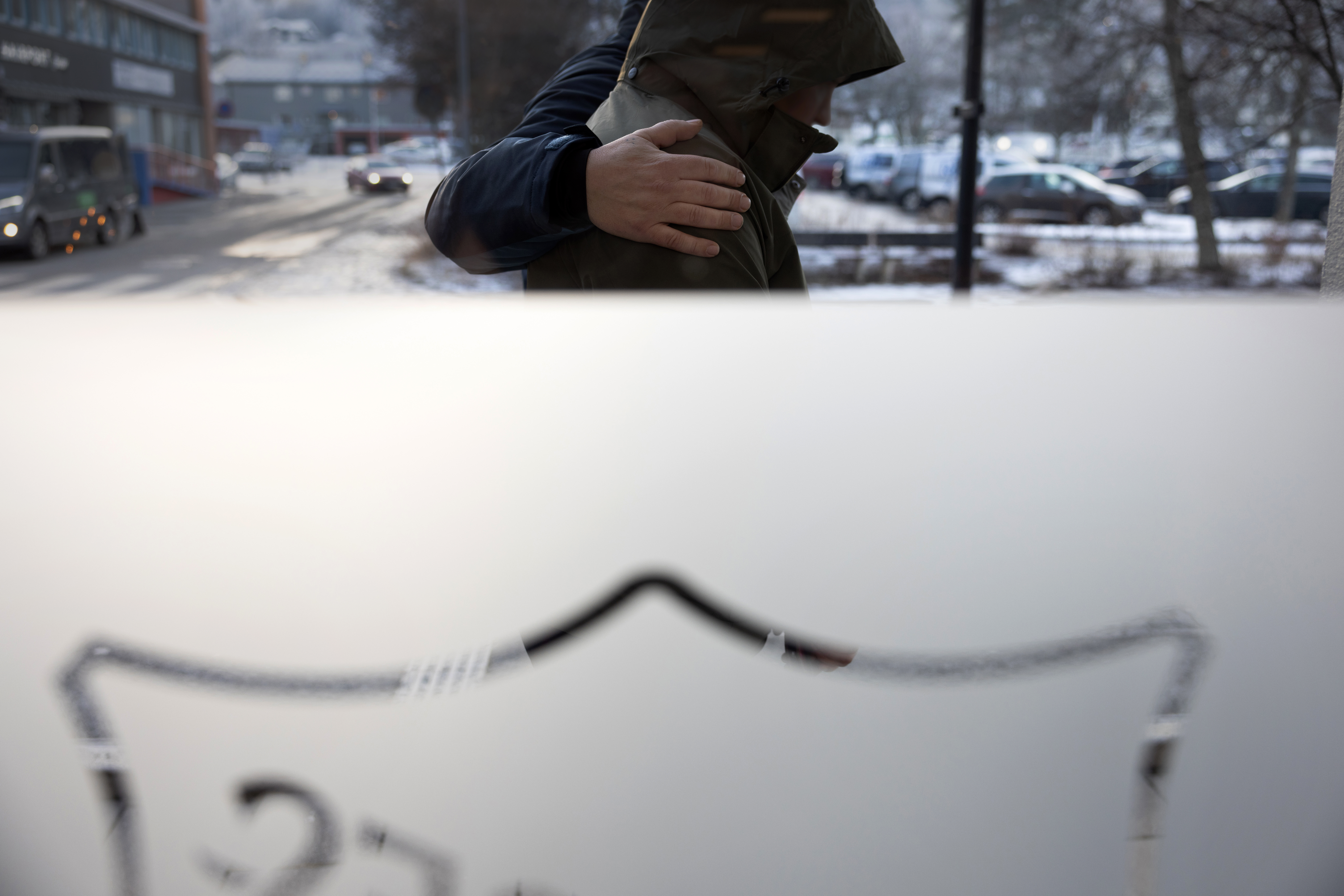 Foto: En mann holder armen rundt en kvinne. De går på utsiden av et bygg til Frelsesarmeen, for logoen i frosta glass er speilvendt. Det er snø og kaldt ute.