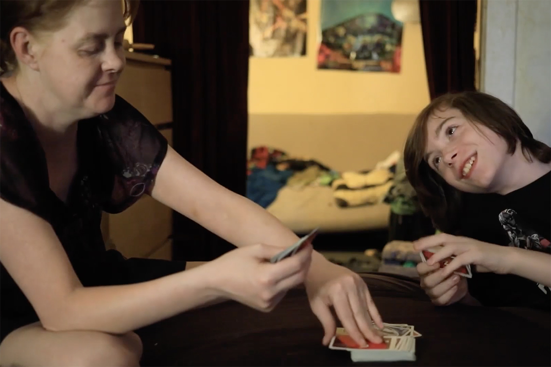 Foto: Kvinne og gutt spiller kort på et hotellrom. De sitter i sengen.