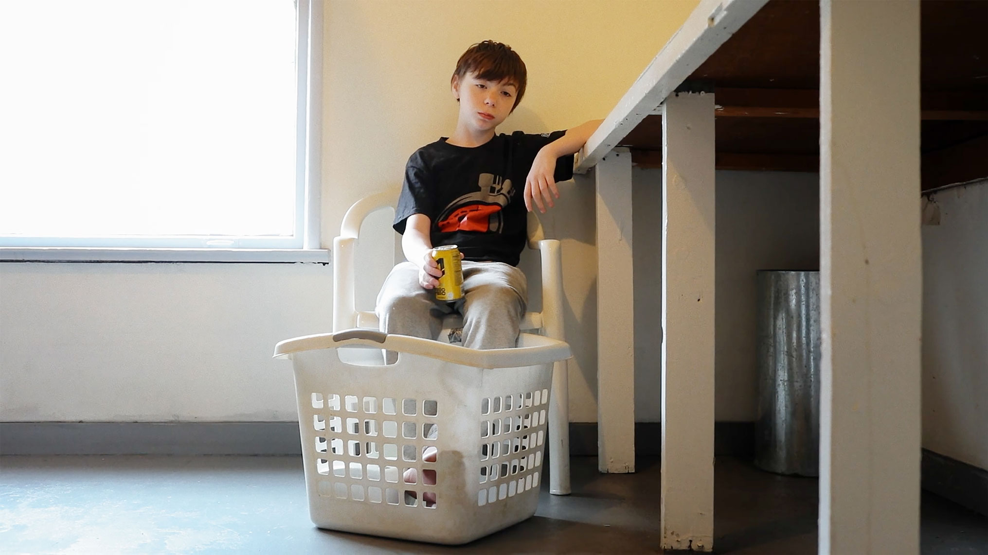 Gutt sitter på et vaskeri med en stor og hvit tom skittentøyskurv foran seg. Han har de nakne beina oppi den. Blikket er tomt. I høyre hånd holder han en brusboks. ´