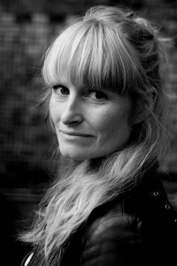 Foto: Svart-hvitt bilde av kvinne med langt lyst hår som snur seg og ser mot kamera.